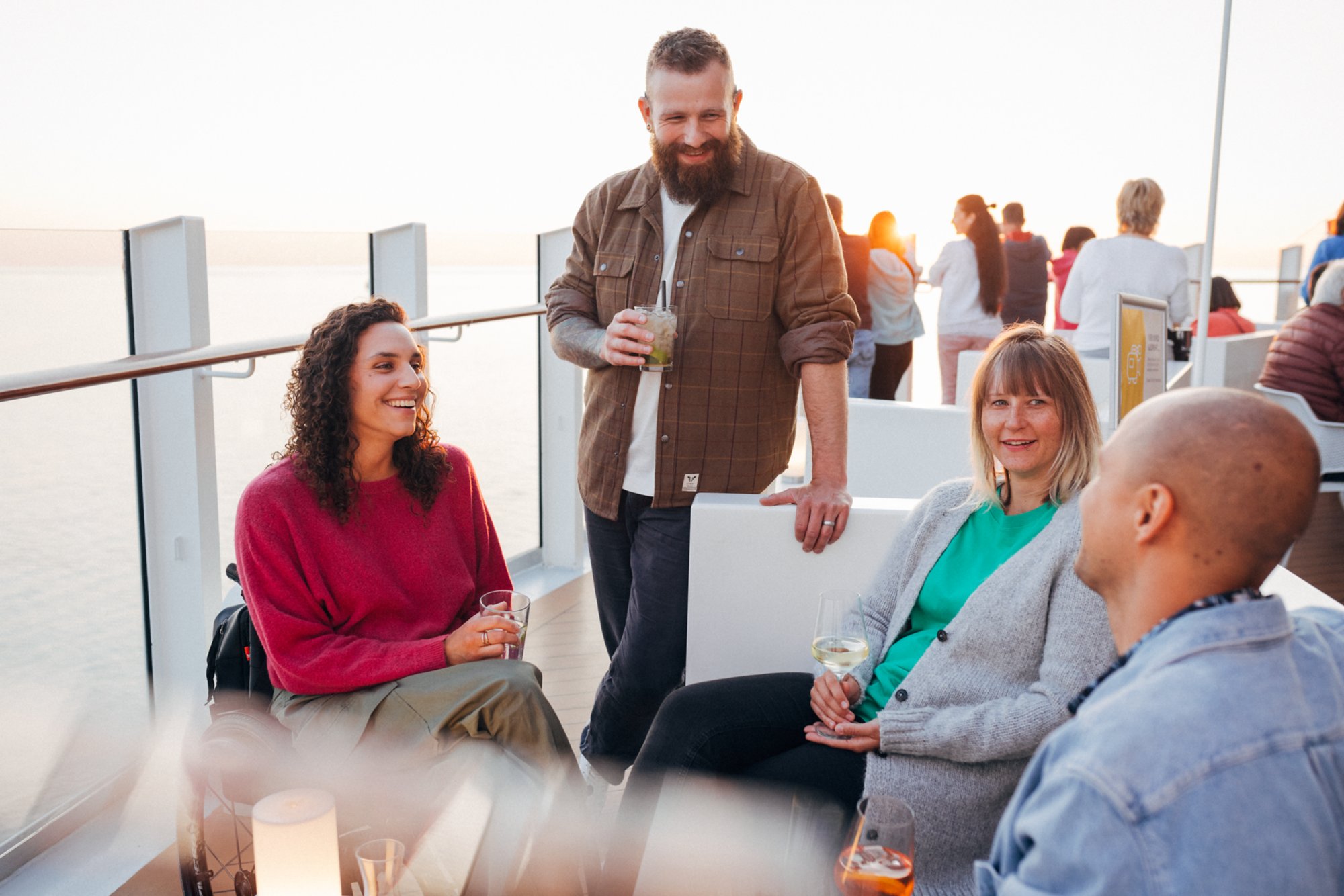 Eine Gruppe von Freunden genießt den Sonnenuntergang auf dem Schiff und trinkt Cocktails.