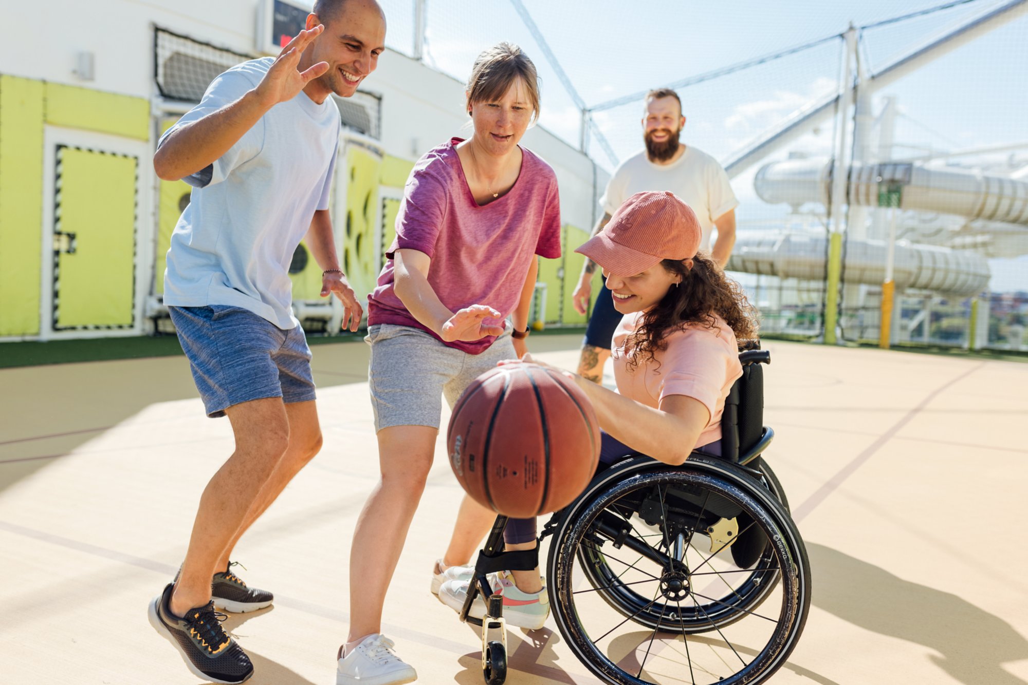 Gruppe spielt Basketball mit Frau in Rollstuhl