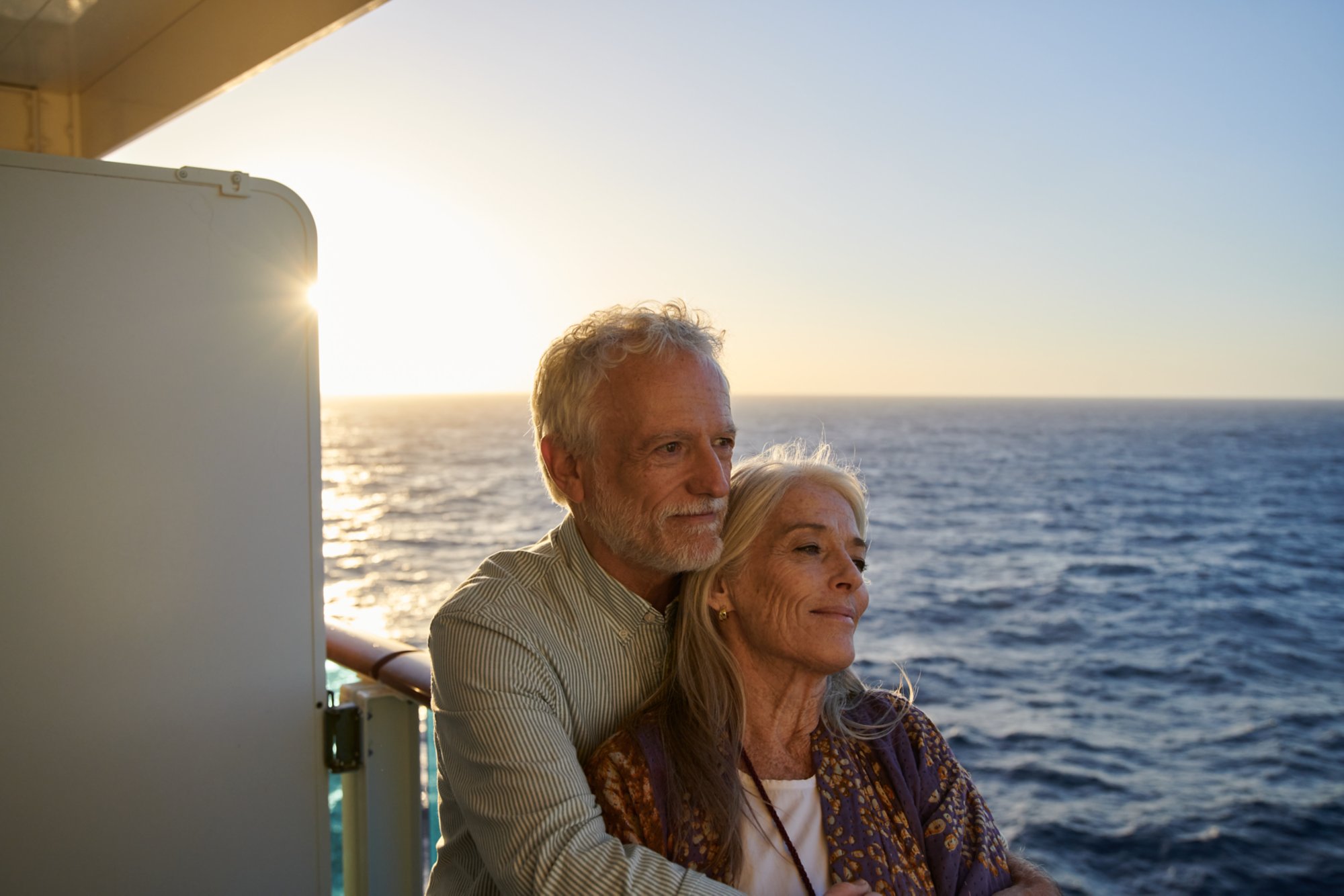 Älteres Paar an der Reling eines Schiffes blickt gemeinsam auf das Meer im Sonnenuntergang 