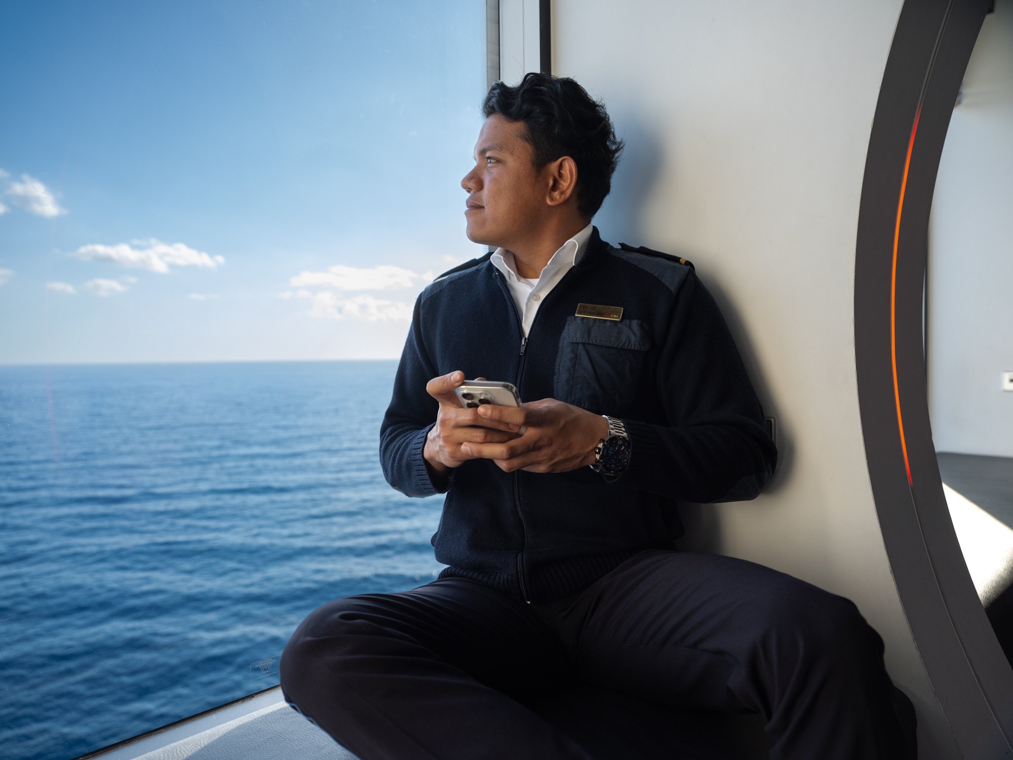 Crew member with mobile phone in hand looking at the sea