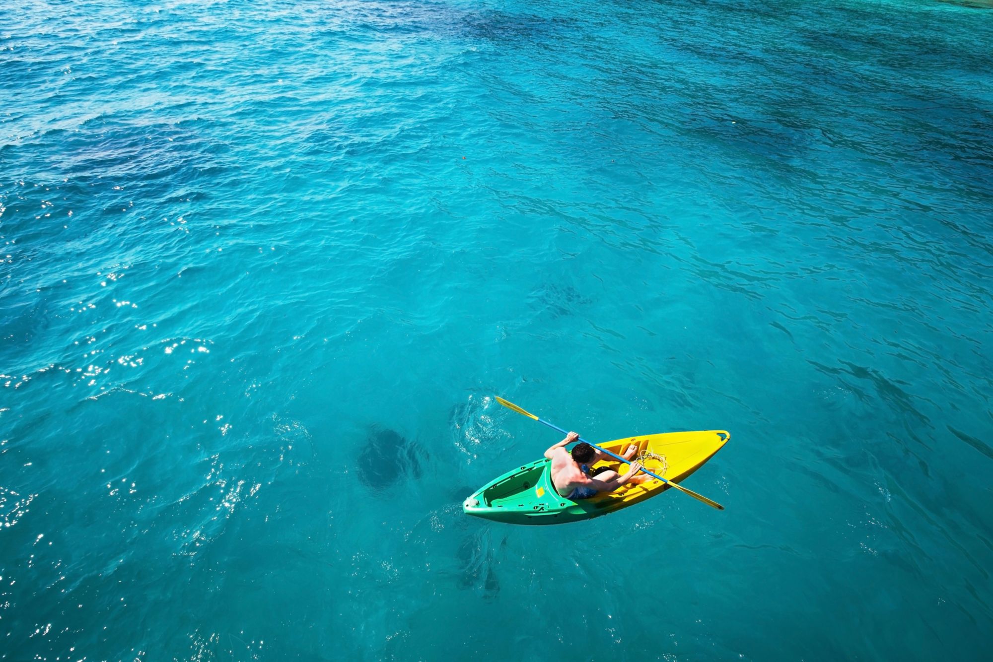 top view of man paddling on kayak in turquoise water
