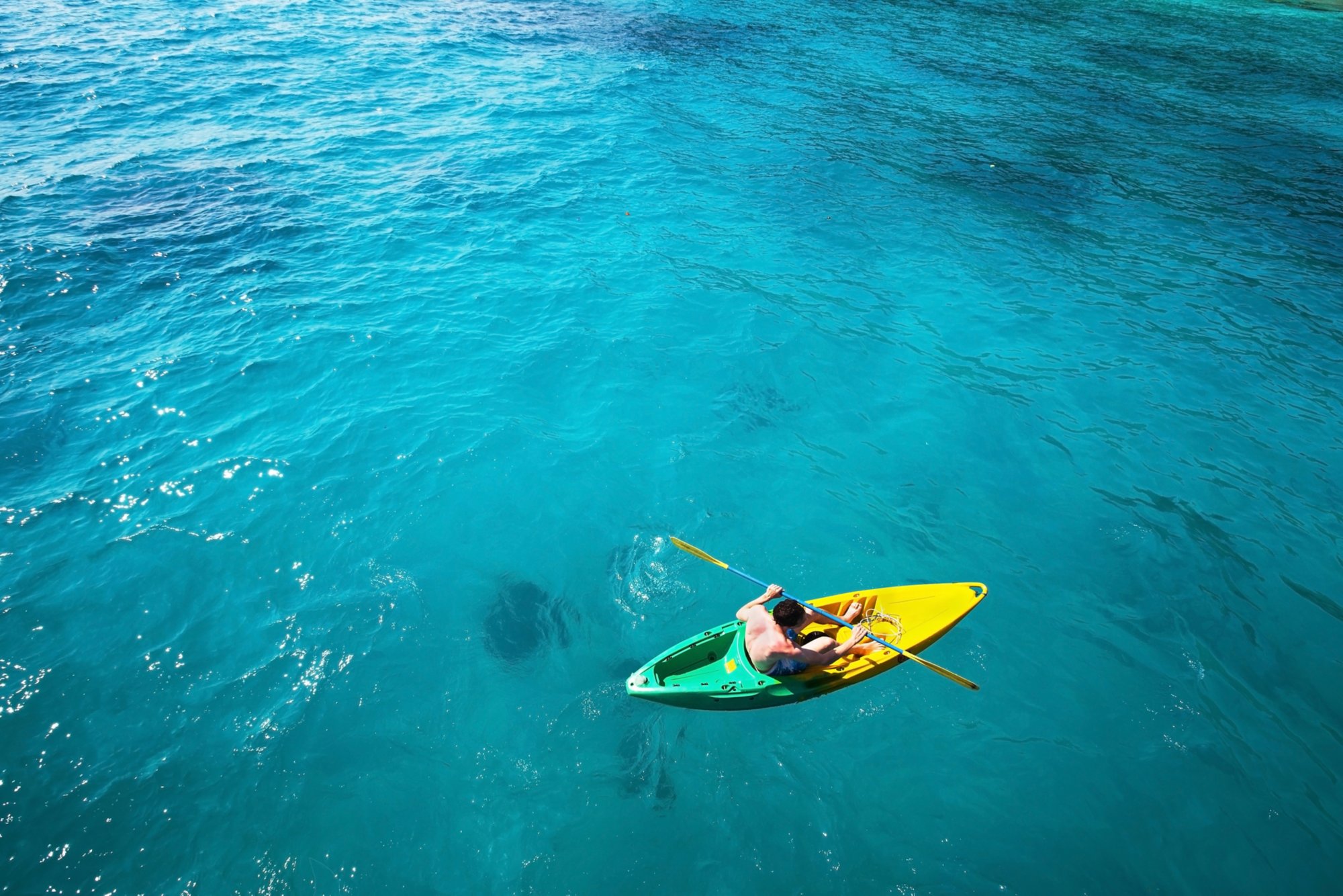 top view of man paddling on kayak in turquoise water