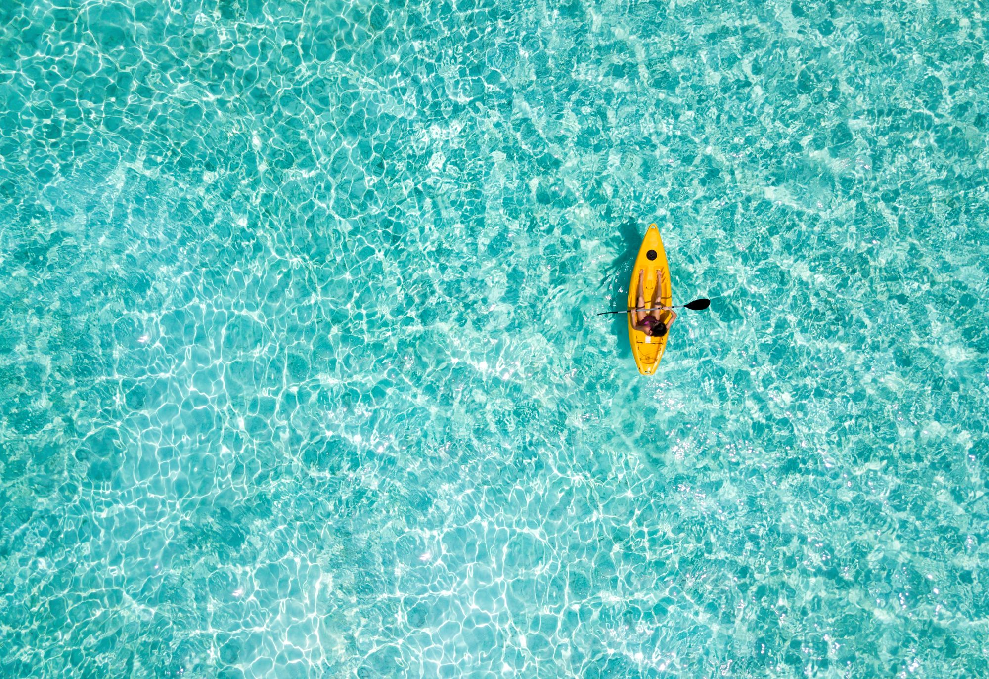 Woman in a canoe over turquoise, tropical waters in the Maldives