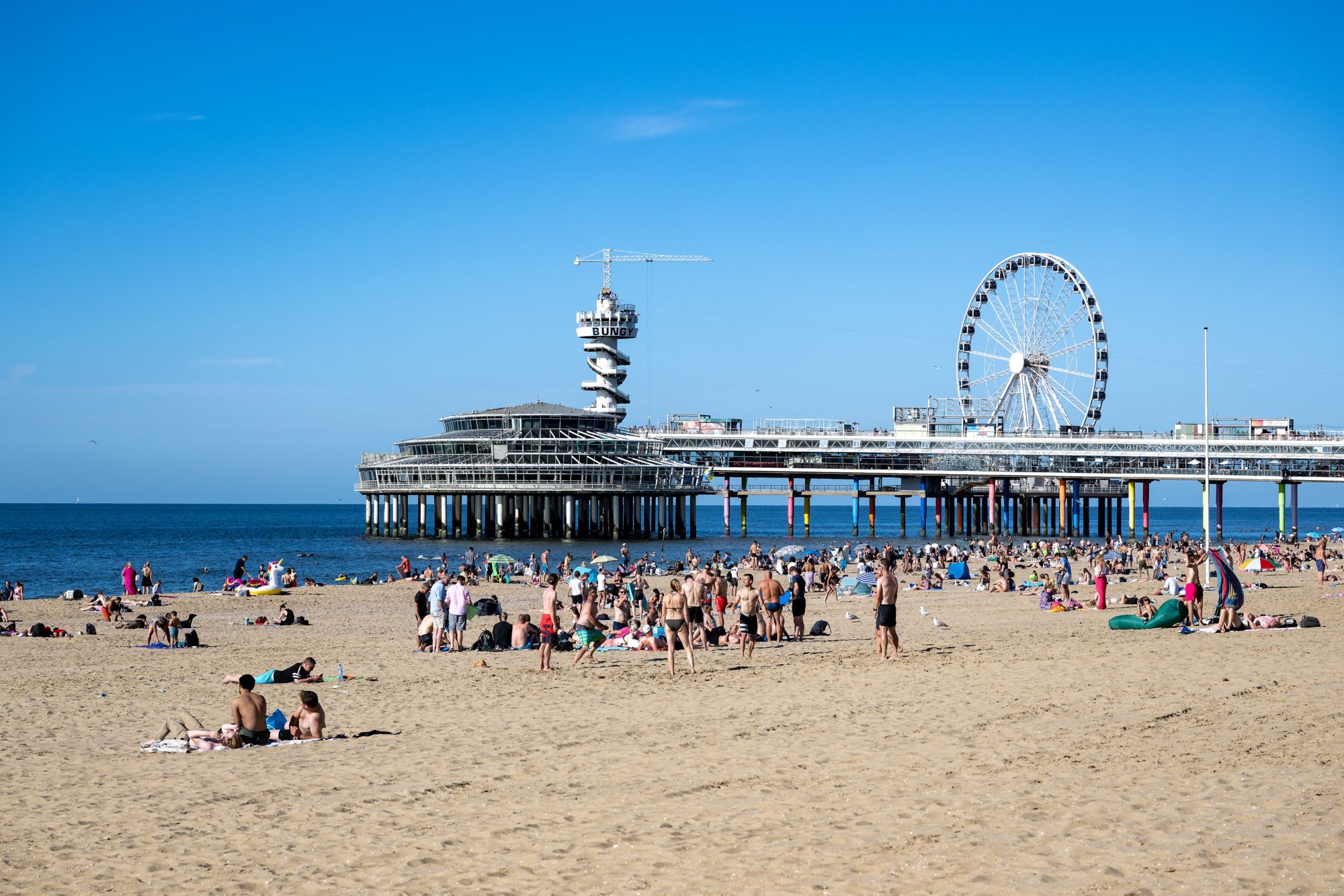 Mensen op het Strand van Scheveningen genieten van het mooie zomerse weer met de Pier en de Noordzee in de achtergrond