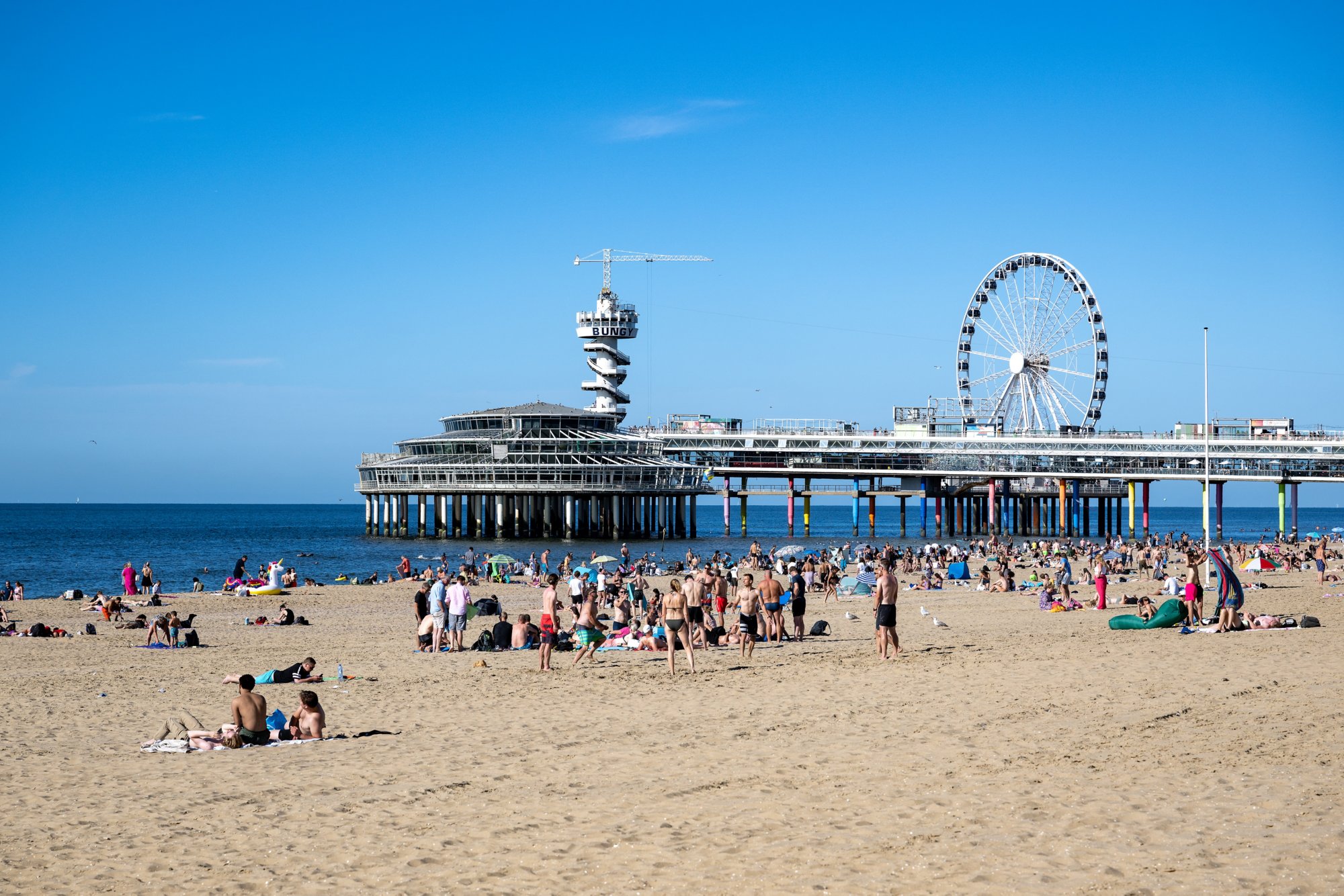 Mensen op het Strand van Scheveningen genieten van het mooie zomerse weer met de Pier en de Noordzee in de achtergrond
