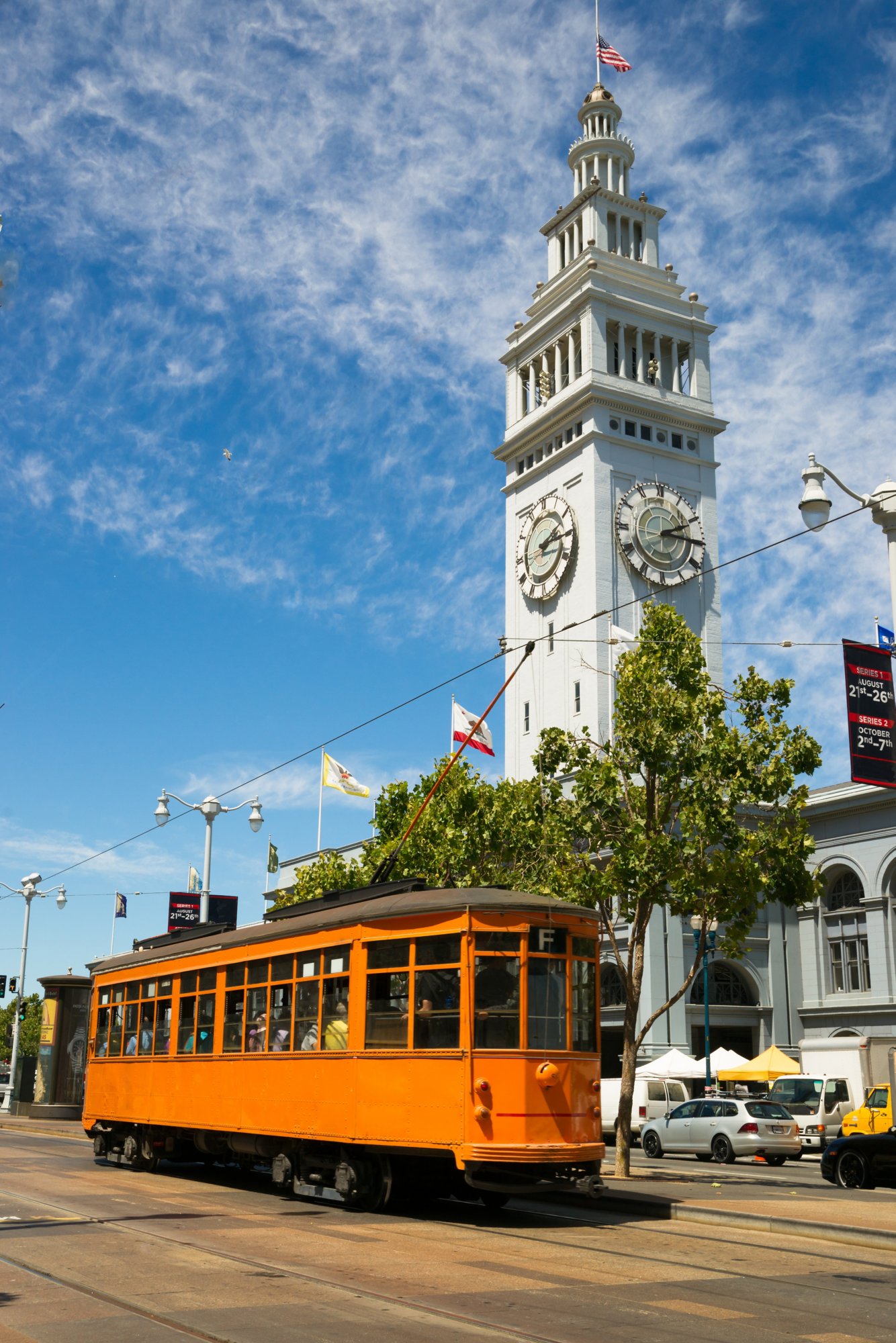 The Ferry Building Clocktower stand in the San Francisco Skyline an Orenge Trolley Foreground