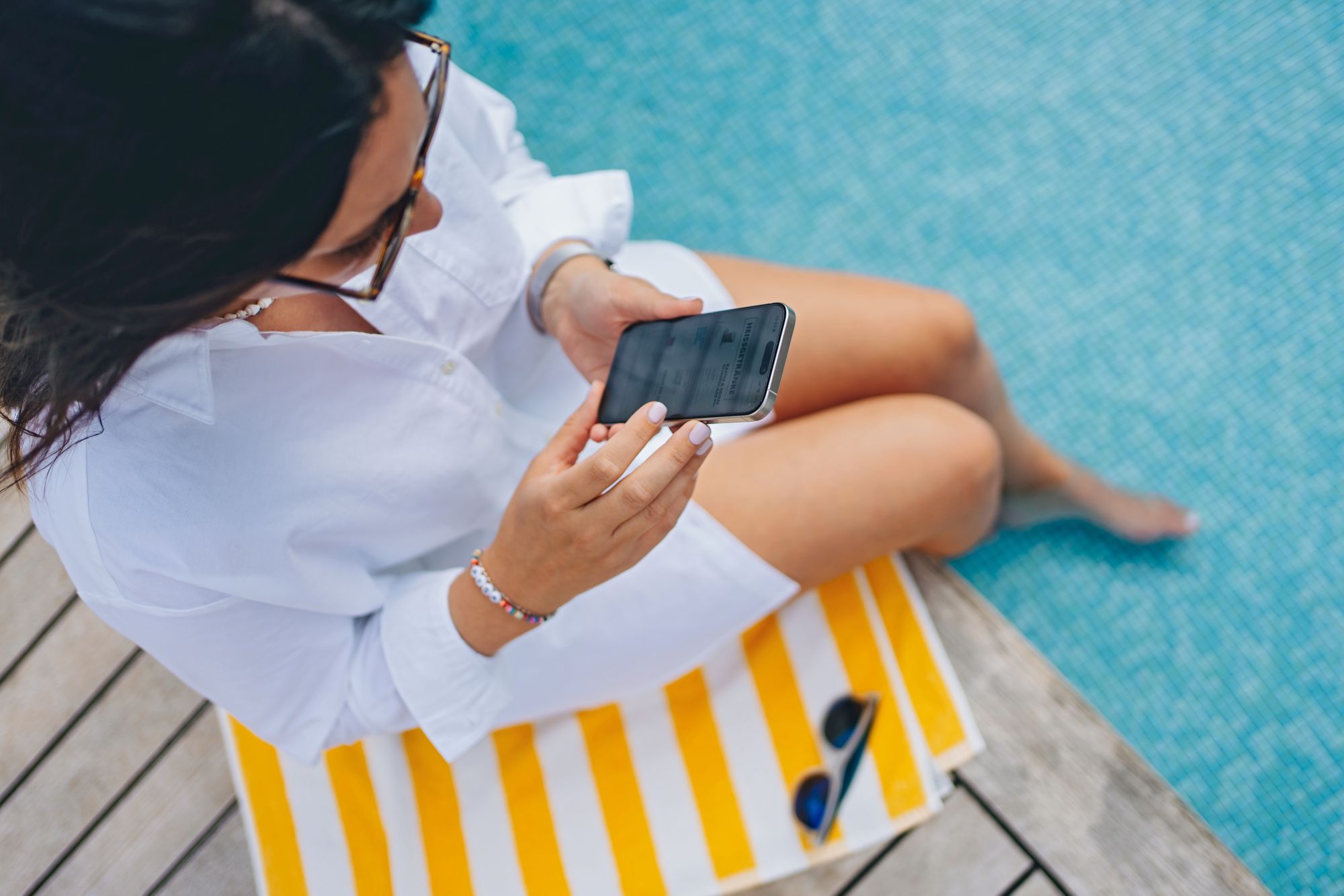 Frau mit Smartphone sitzt am Pool
