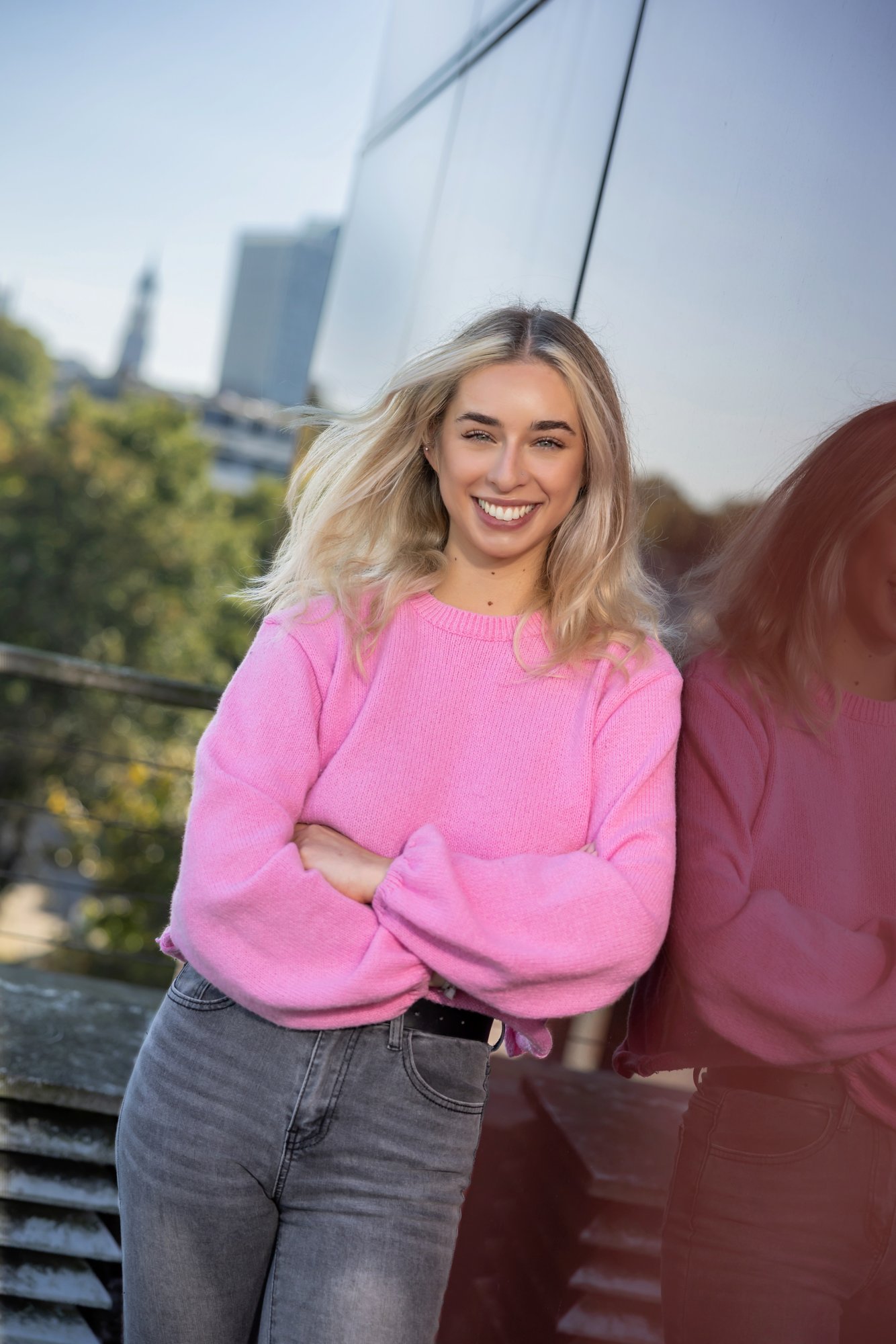 Junge Frau mit blonden schulterlangen Haare und Brille. Sie trägt ein fliederfarbenes T-Shirt, darüber eine beige Jacke. Sie lächelt in die Kamera und hält ein altes Radio in den Händen.