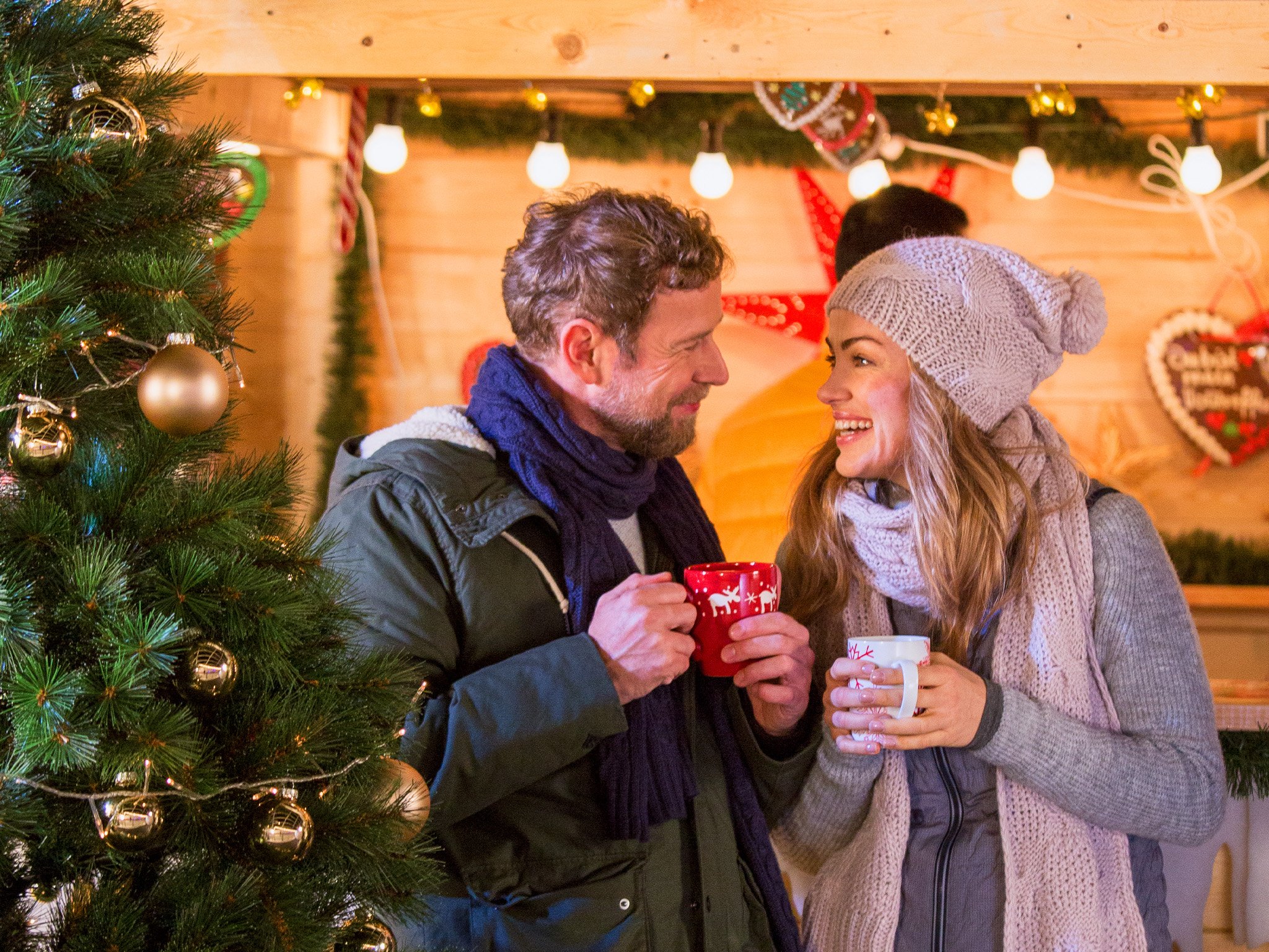 Paar mit Heißgetränk am Weihnachtsmart-Stand in winterlichen Outfits 