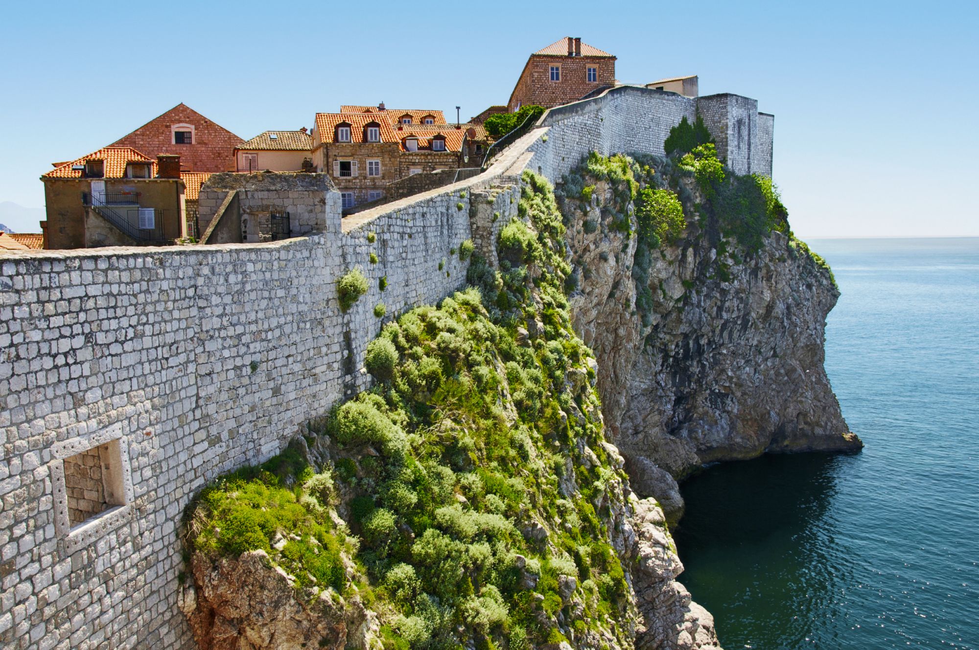 Stadtmauer von Dubrovnik mit Blick auf die Adria und historische Gebäude mit roten Ziegeldächern.“