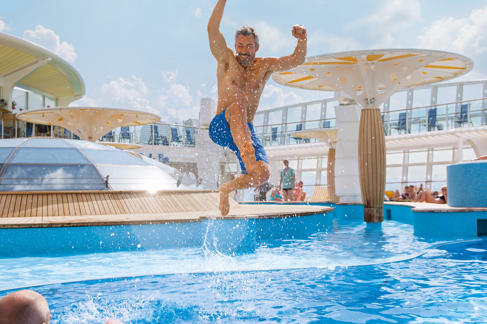 Ein Mann mit blauer Badehose springt in den Pool