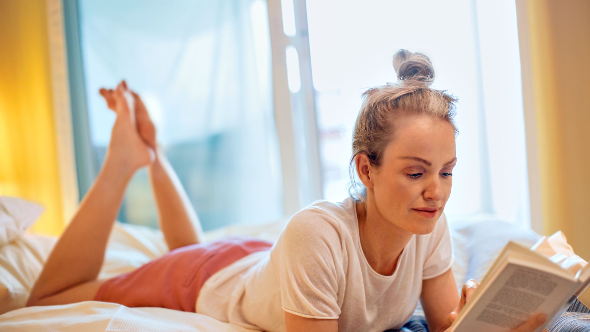 Frau liegt mit Buch auf Bett