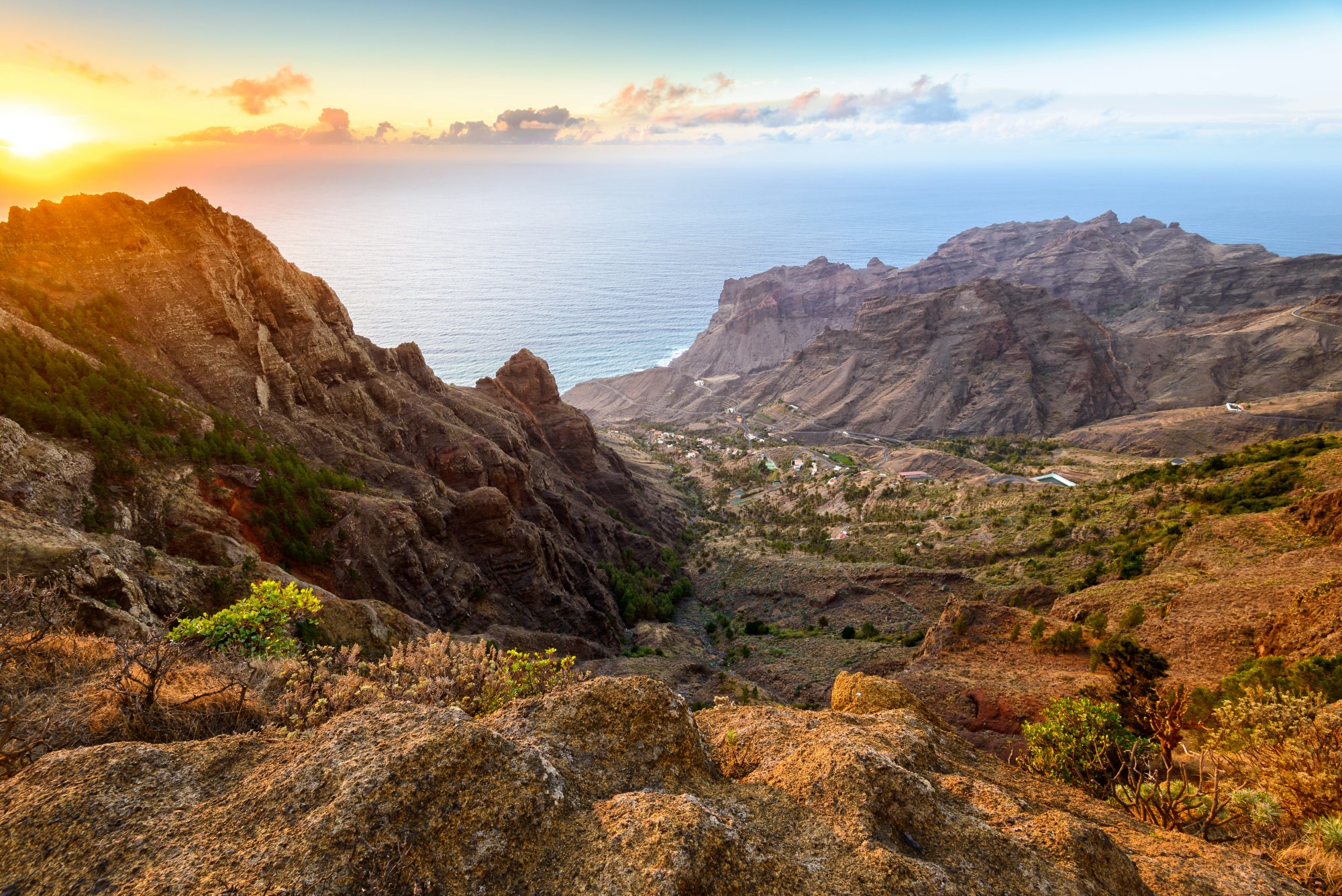 Blick auf begrünte Canyons und steile Felswände mit einem traumhaften Sonnenuntergang am Horizont auf La Gomera