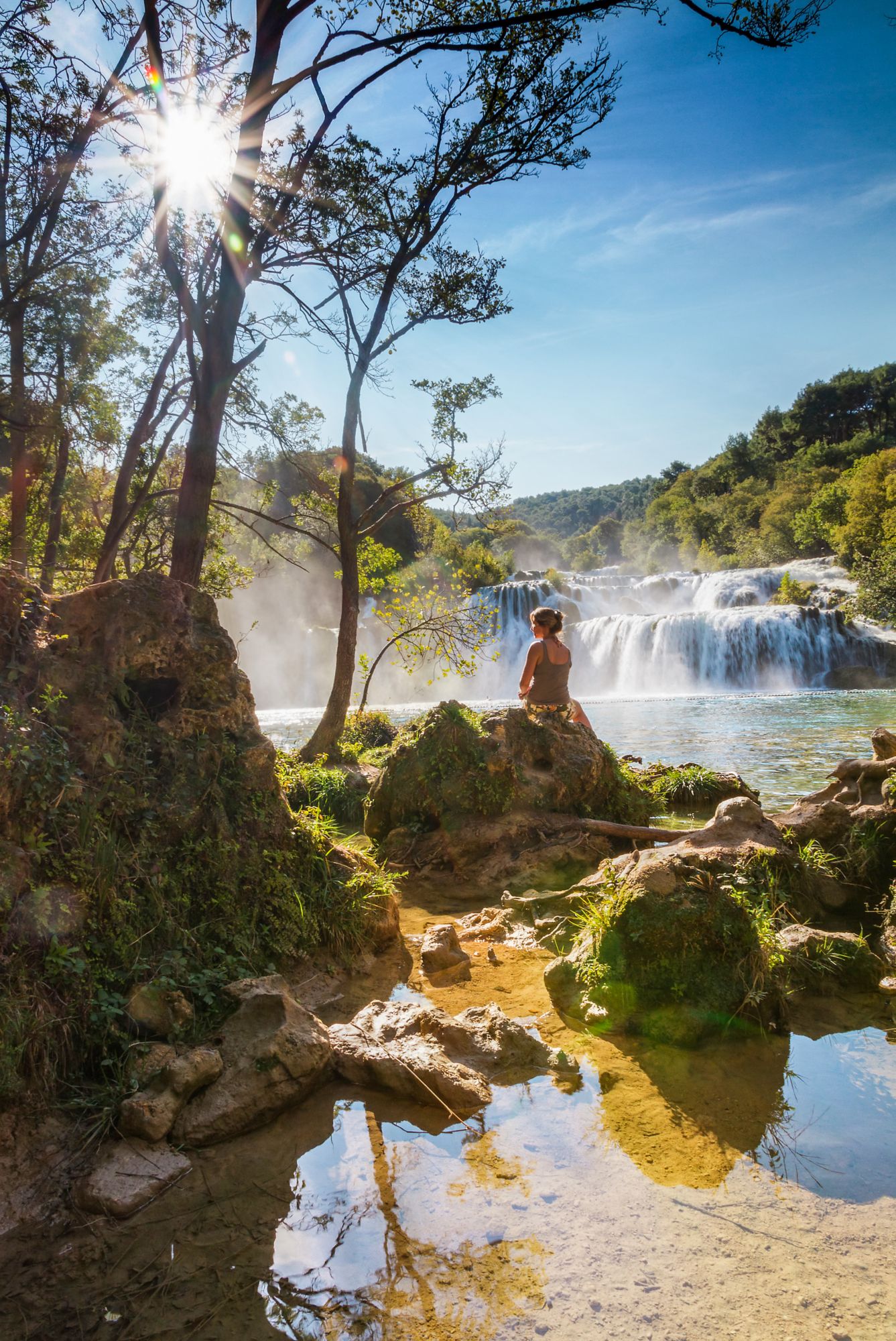 Beautiful woman sits at the waterfall in Krka national park, Croatia