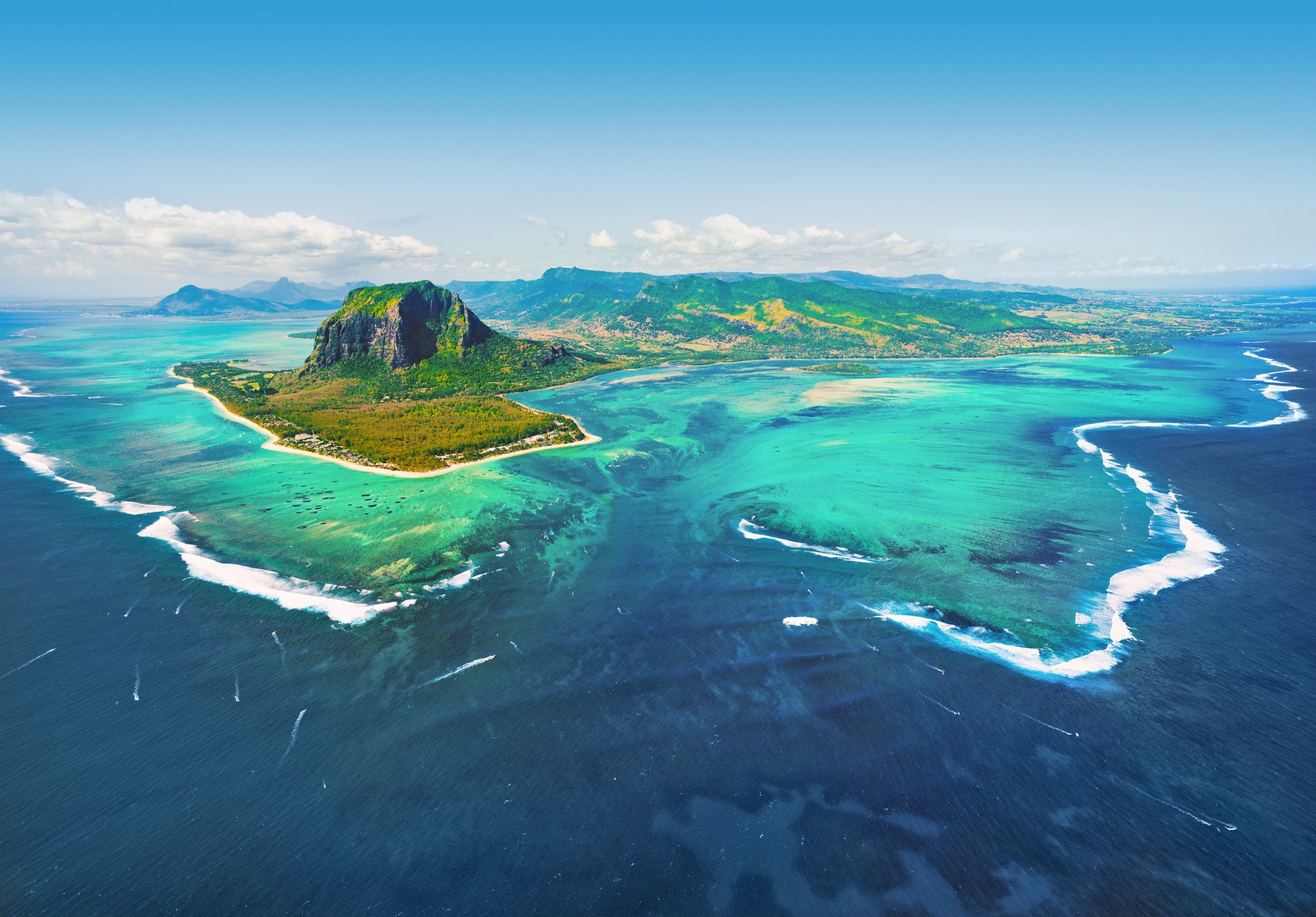 Tropische Insel mit grünem Hügel, weißen Stränden und umgeben von türkisfarbenem Wasser und Korallenriffen aus der Vogelperspektive