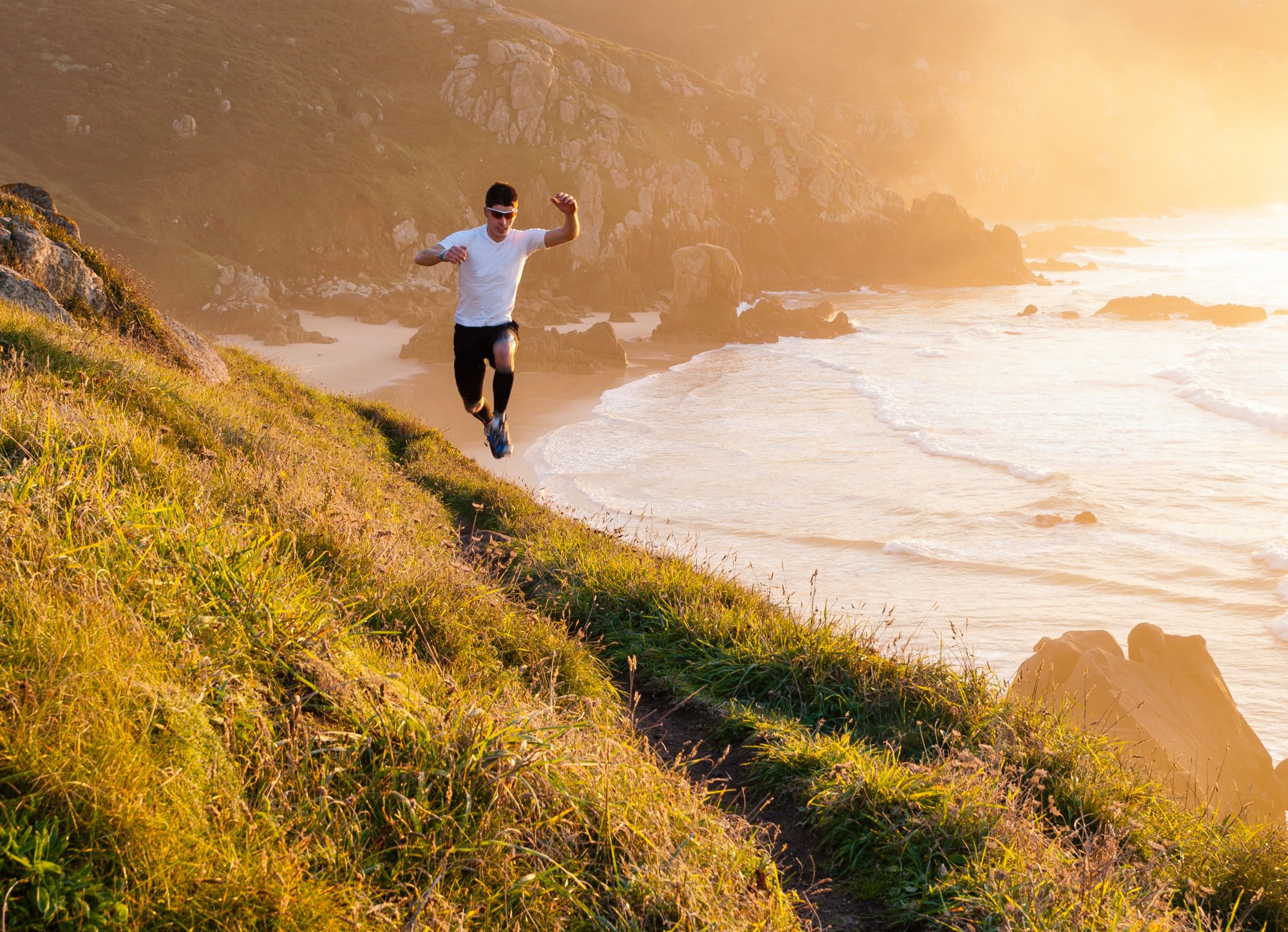 Man practicing trail running and leaping in a path in the coast in a sunny day