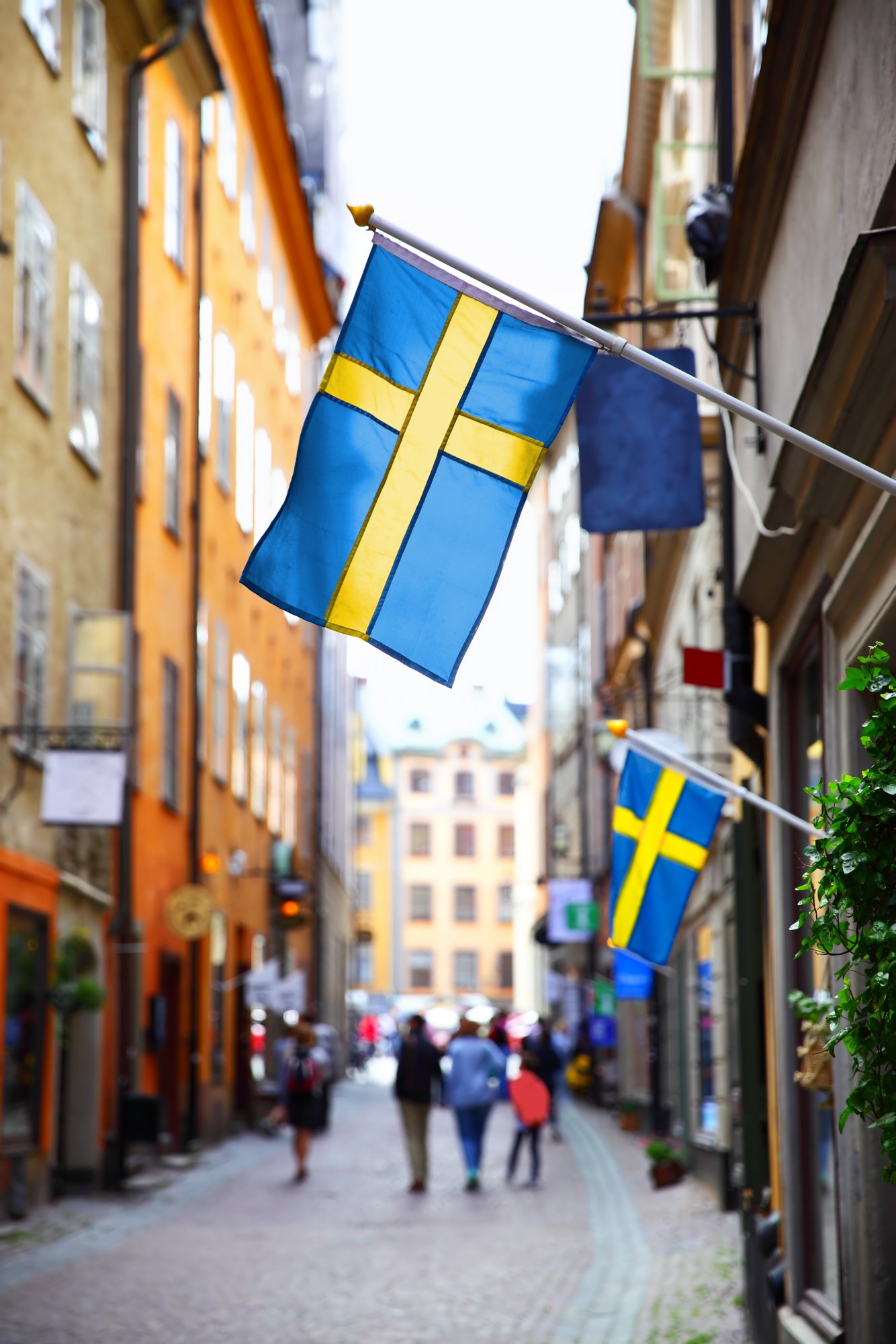 Perspective of old street in Stockholm with swedish flags, Sweden. Shallow DOF, focus on the first flag