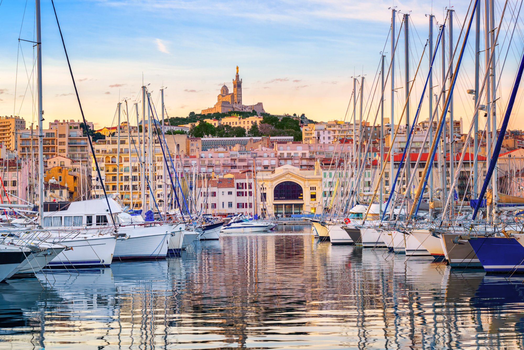 Yachts reflecting in the still water of the old Vieux Port of Marseilles beneath Cathedral of Notre Dame, France, on sunrise