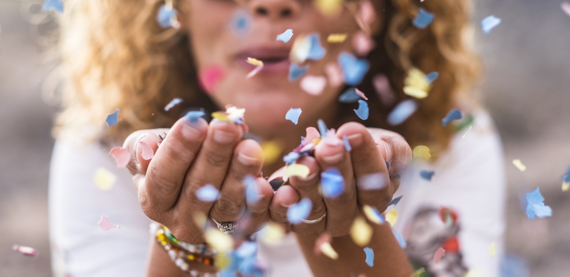 beautiful defocused woman blow confetti from hands. celebration and event concept. happiness and coloured image. movement and ahppiness having fun