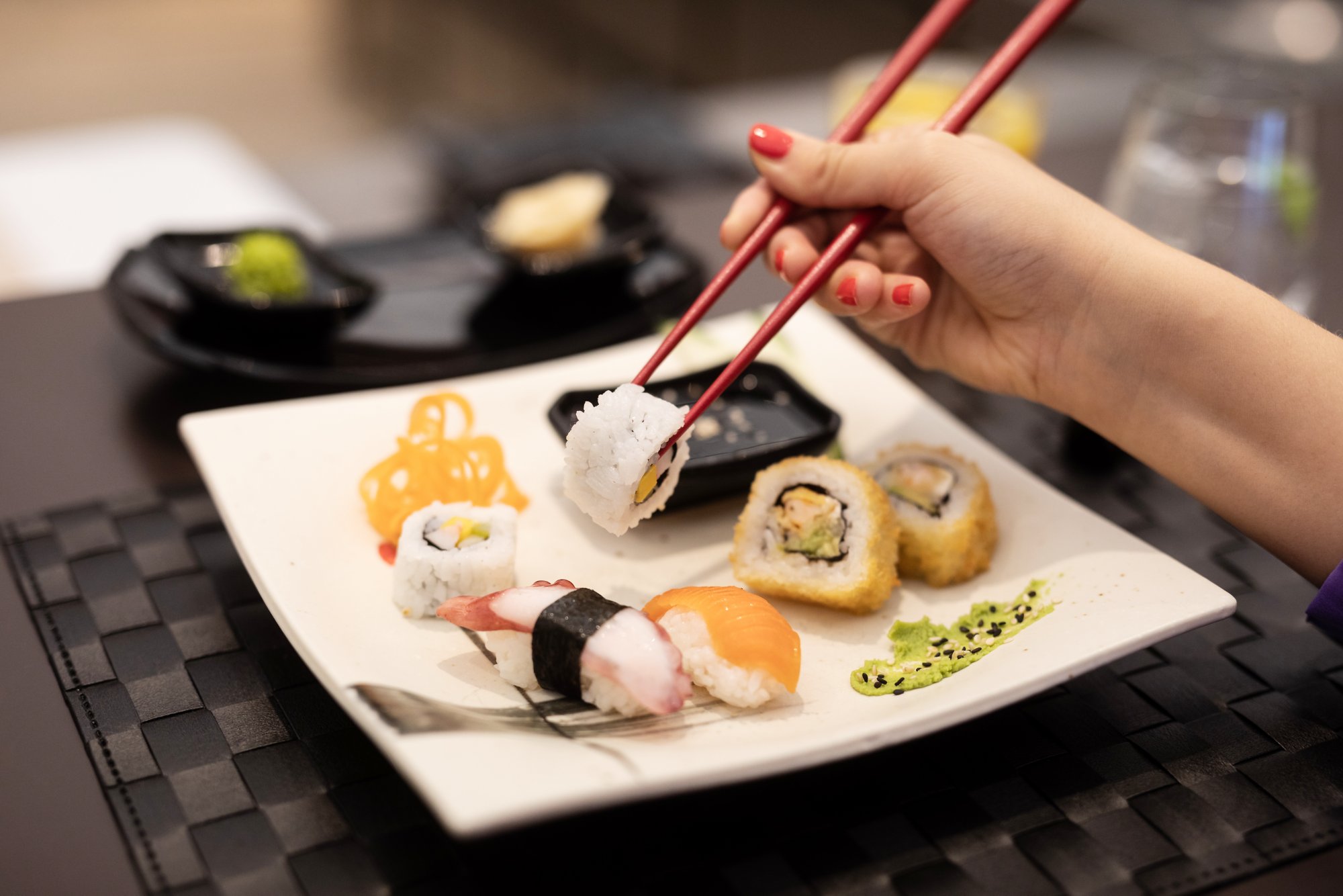 Sushi Platte: Person nimmt sich mit Stäbchen ein Stück