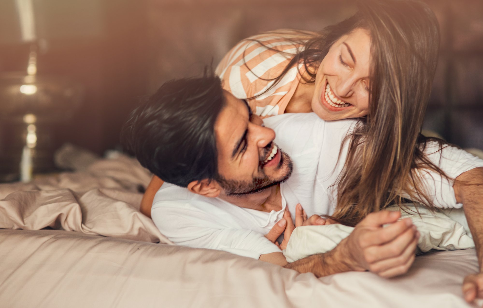 Happy young playful couple in bed.