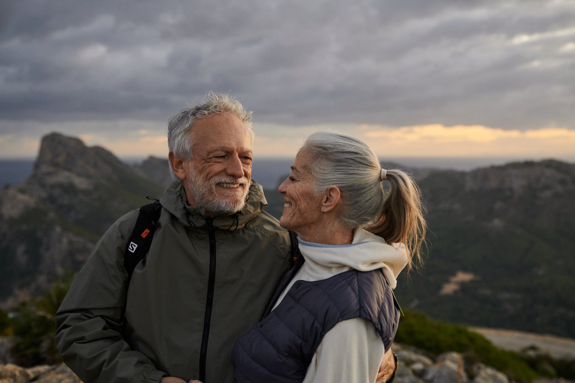 Älteres Paar in Outdoor-Bekleidung steht vor einer Bergkulisse