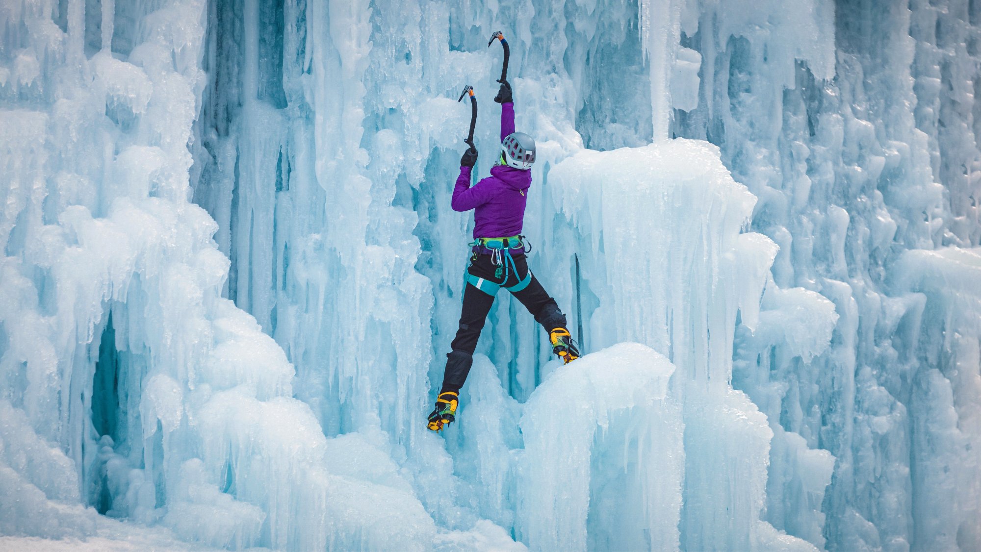 Alpinist woman with ice climbing equipment on a frozen waterfall