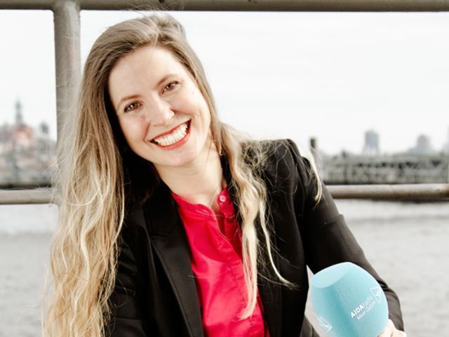 Arne Waack steht an einem Geländer, trägt ein gestreiftes T-Shirt, darüber eine Jacke. Auf dem Kopf hat er eine Seefahrermütze, die die Ohren nicht bedeckt, er lächelt