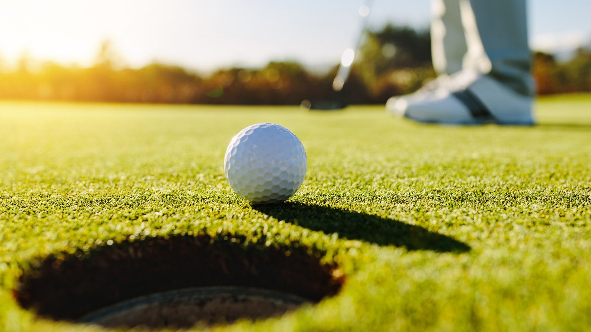 Professional golfer putting ball into the hole. Golf ball by the edge of hole with player in background on a sunny day.