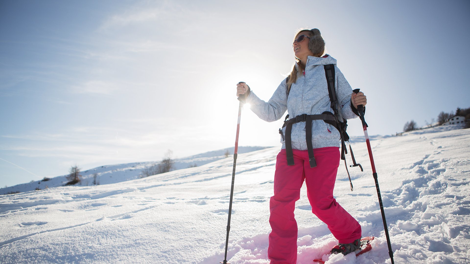 A woman snowshoeing in winter with all sport clothing equipment during a beautiful sunny day, going the way down,sun behind her.Winter in Switzerland.