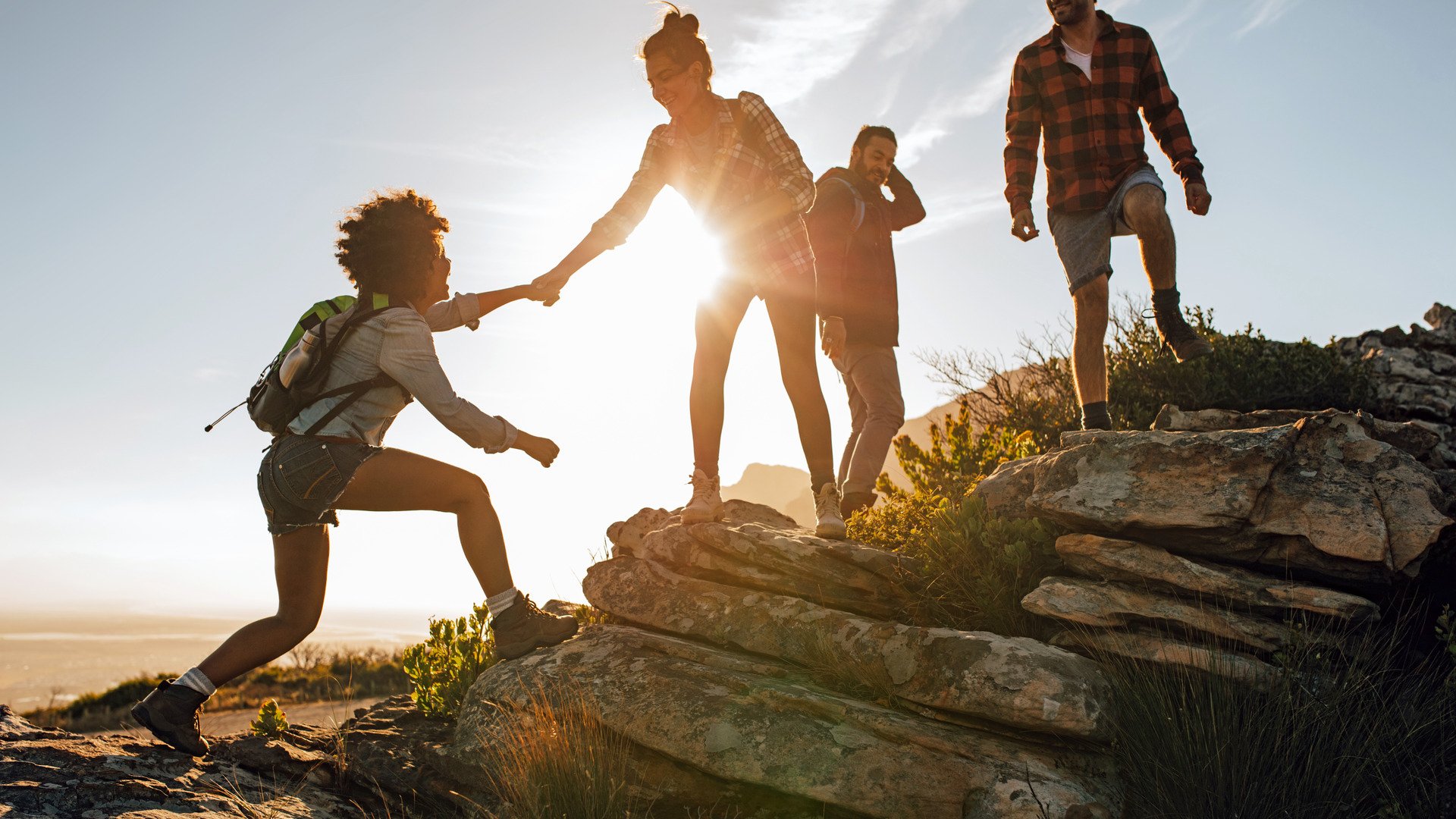 Group of hikers on a mountain. Woman helping her friend to climb a rock. Young people on mountain hike at sunset.
