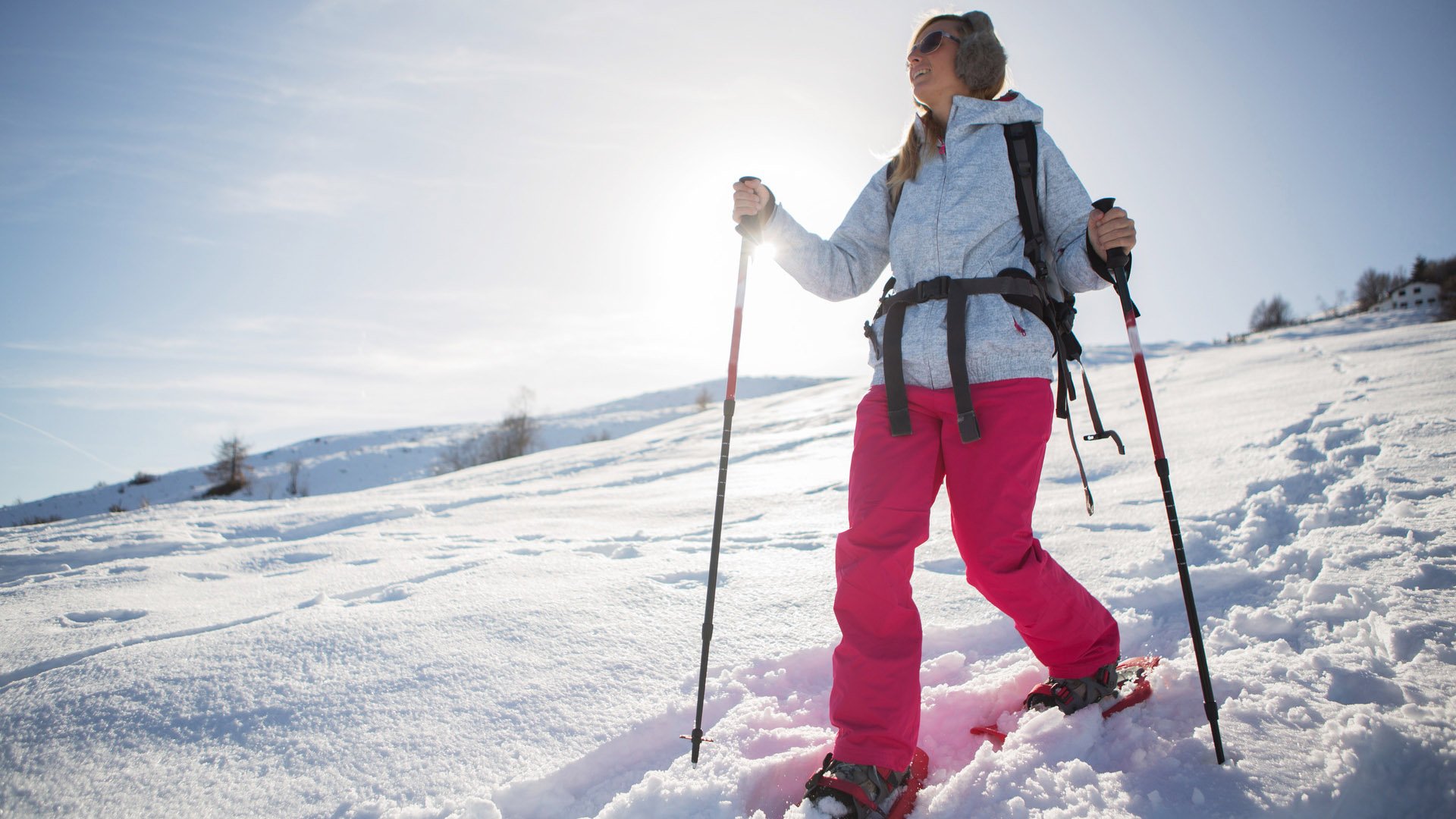 A woman snowshoeing in winter with all sport clothing equipment during a beautiful sunny day, going the way down,sun behind her.Winter in Switzerland.