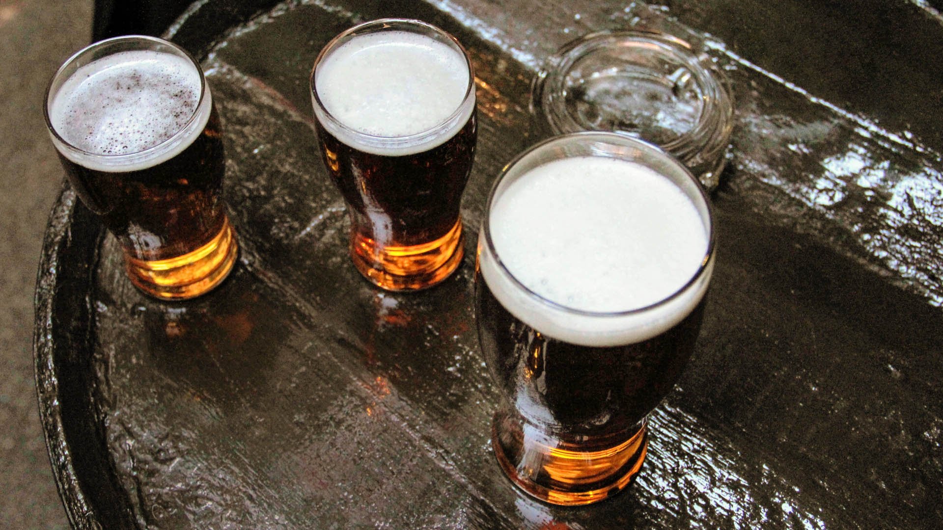 Three pints of lager beer viewed from above on a brown barrel outside of a pub or a bar, and an ashtray; Shutterstock ID 792799453