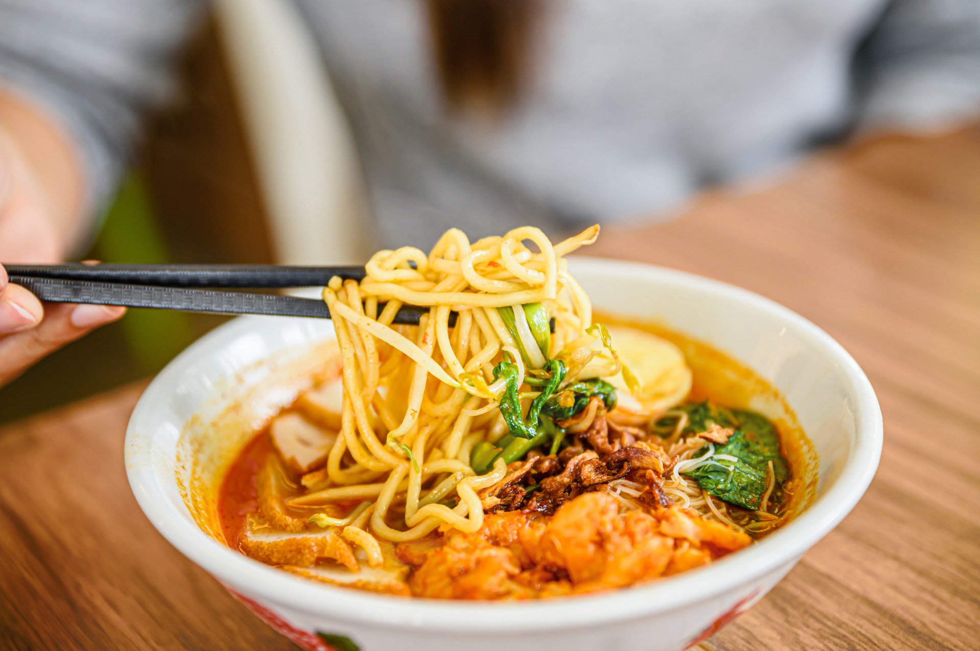 Hand with Chinese chopsticks eating noodle, a famous Malaysia prawn noodle cerry soup.