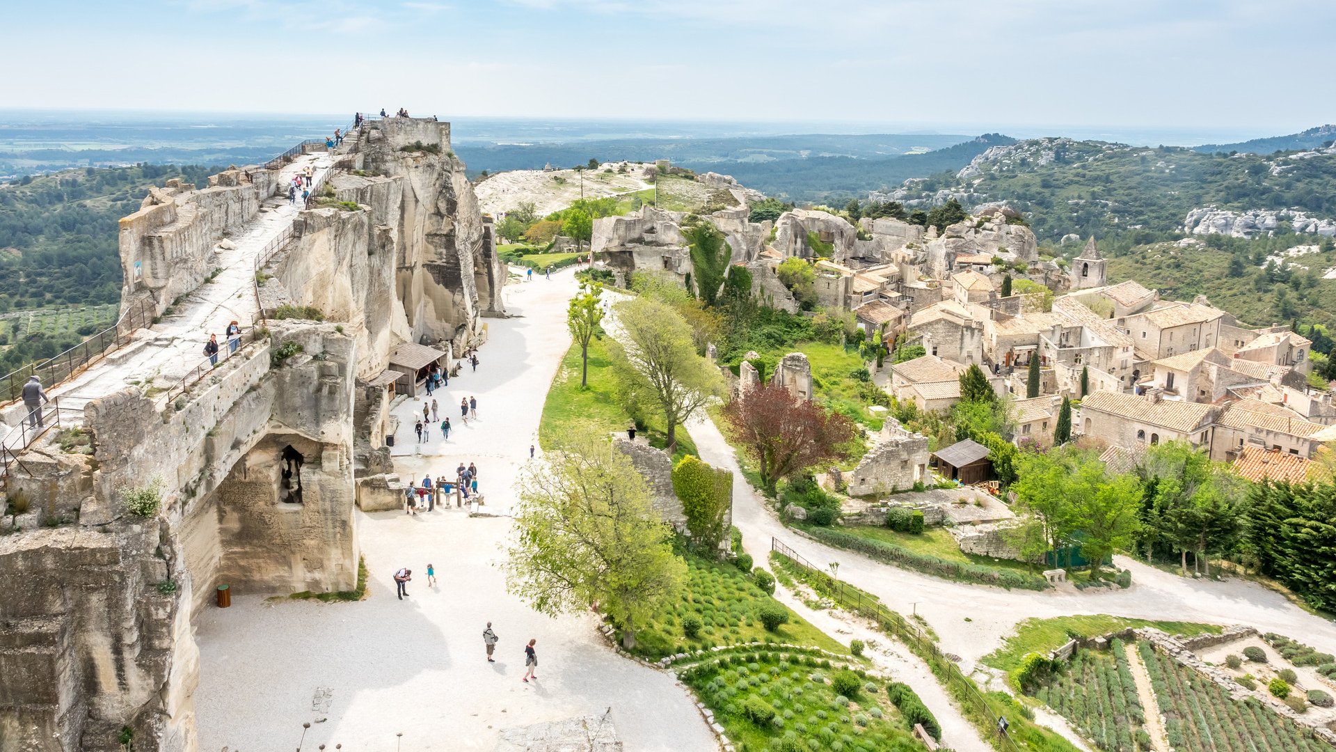 Lower courtyards of area around Chateau des Baux-de-provence in france with unrecognized tourists, under cloudy blue sky