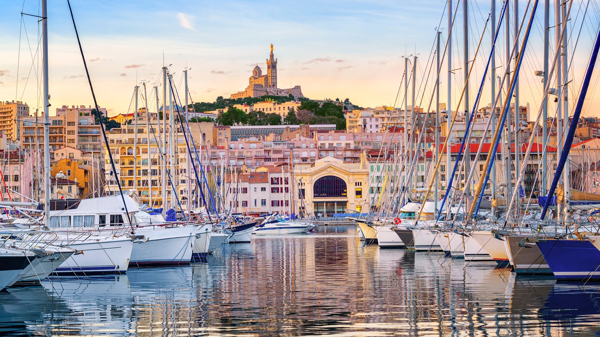 Yachts reflecting in the still water of the old Vieux Port of Marseilles beneath Cathedral of Notre Dame, France, on sunrise