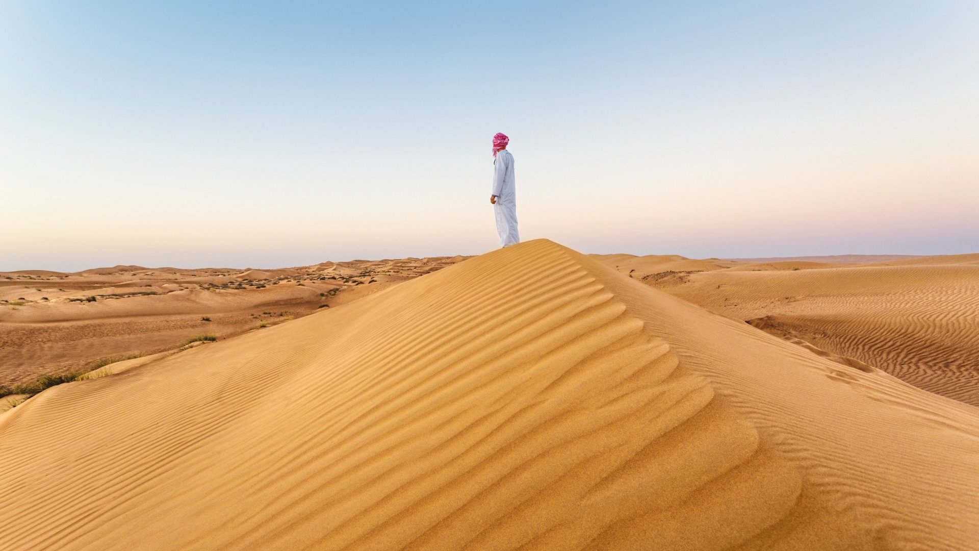 Omani man with traditional clothing, looking at sunrise in the desert, Wahiba sands, Oman.