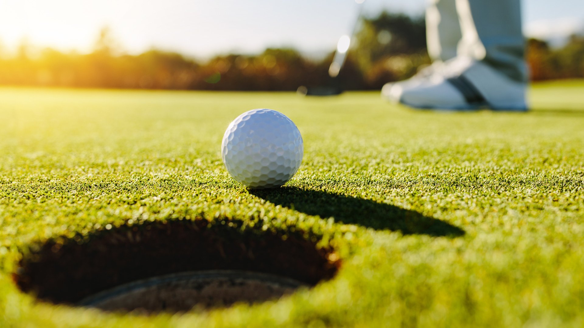 Professional golfer putting ball into the hole. Golf ball by the edge of hole with player in background on a sunny day.