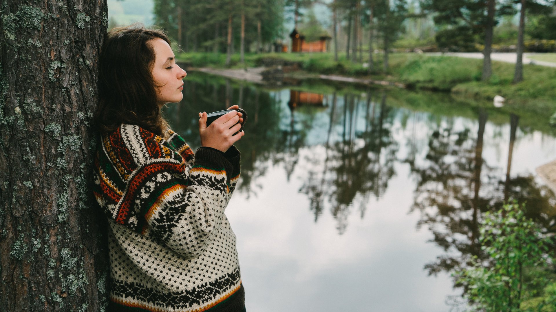 Young Caucasian woman drinking tea  near the lake in forest in Norway