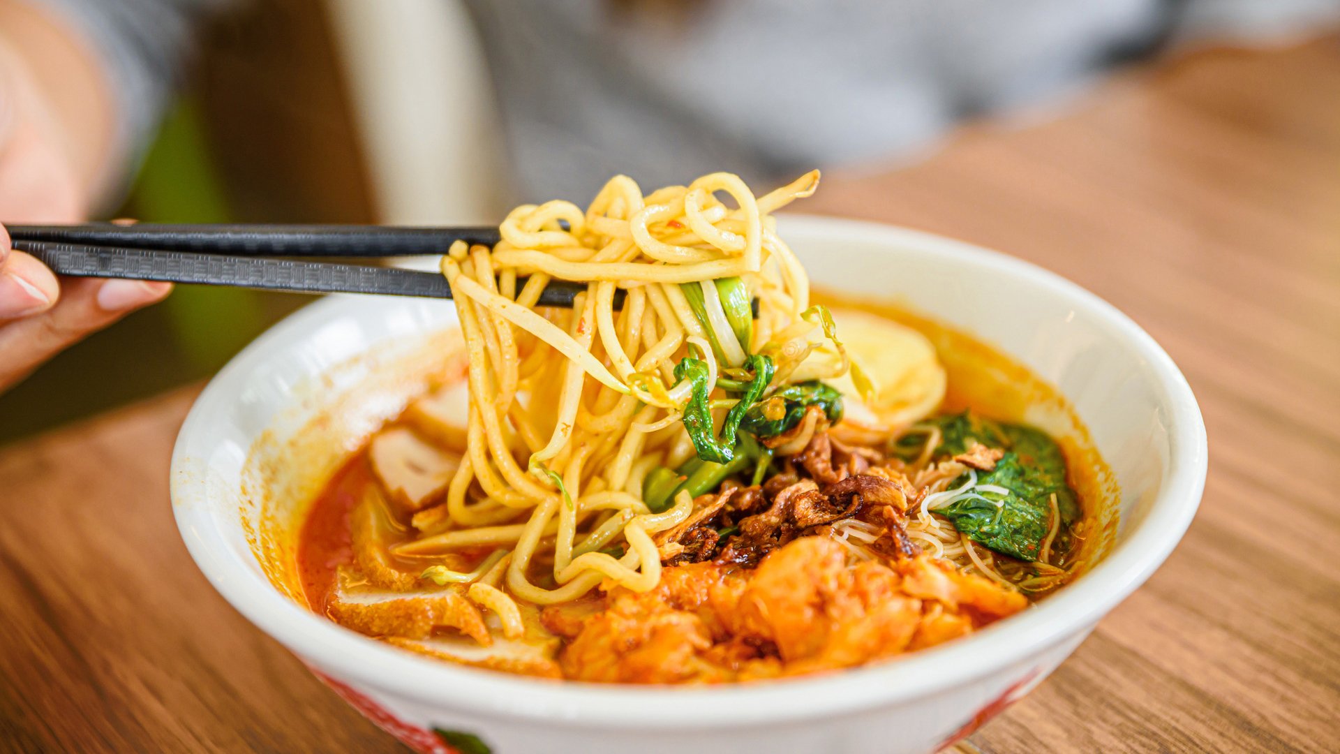 Hand with Chinese chopsticks eating noodle, a famous Malaysia prawn noodle cerry soup.