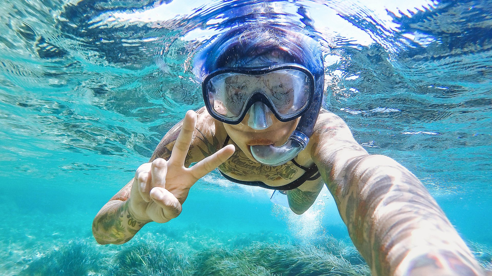 Young woman swimming with mask snorkeling in the Balearic Sea of Balearic Island. Showing victory signal.