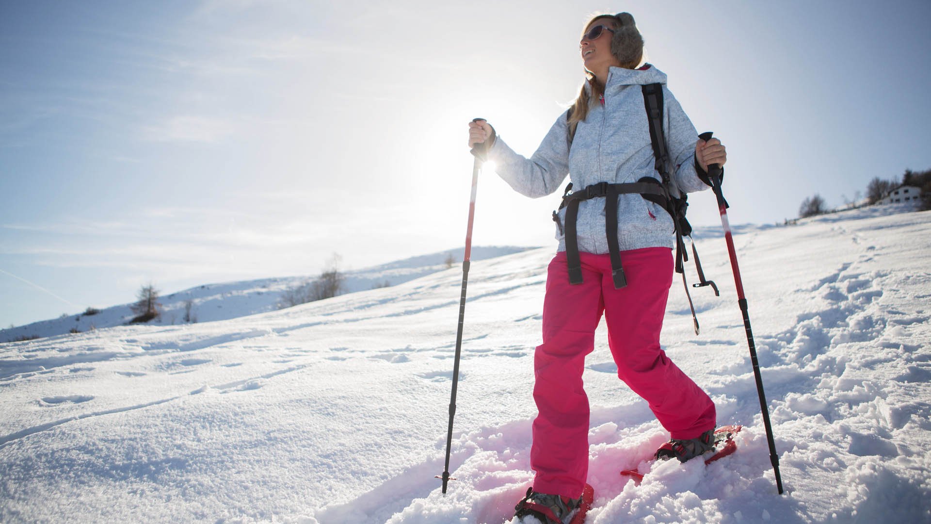 A woman snowshoeing in winter with all sport clothing equipment during a beautiful sunny day, going the way down,sun behind her.Winter in Switzerland.