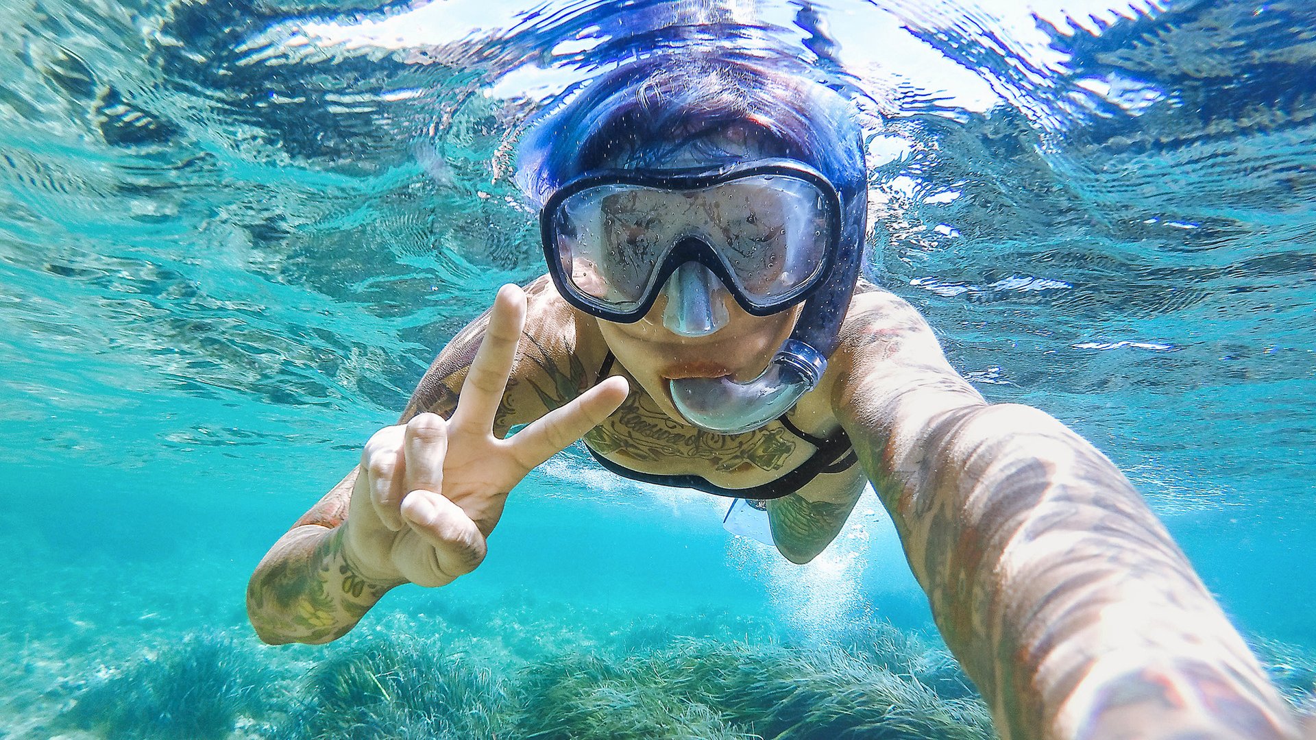 Young woman swimming with mask snorkeling in the Balearic Sea of Balearic Island. Showing victory signal.