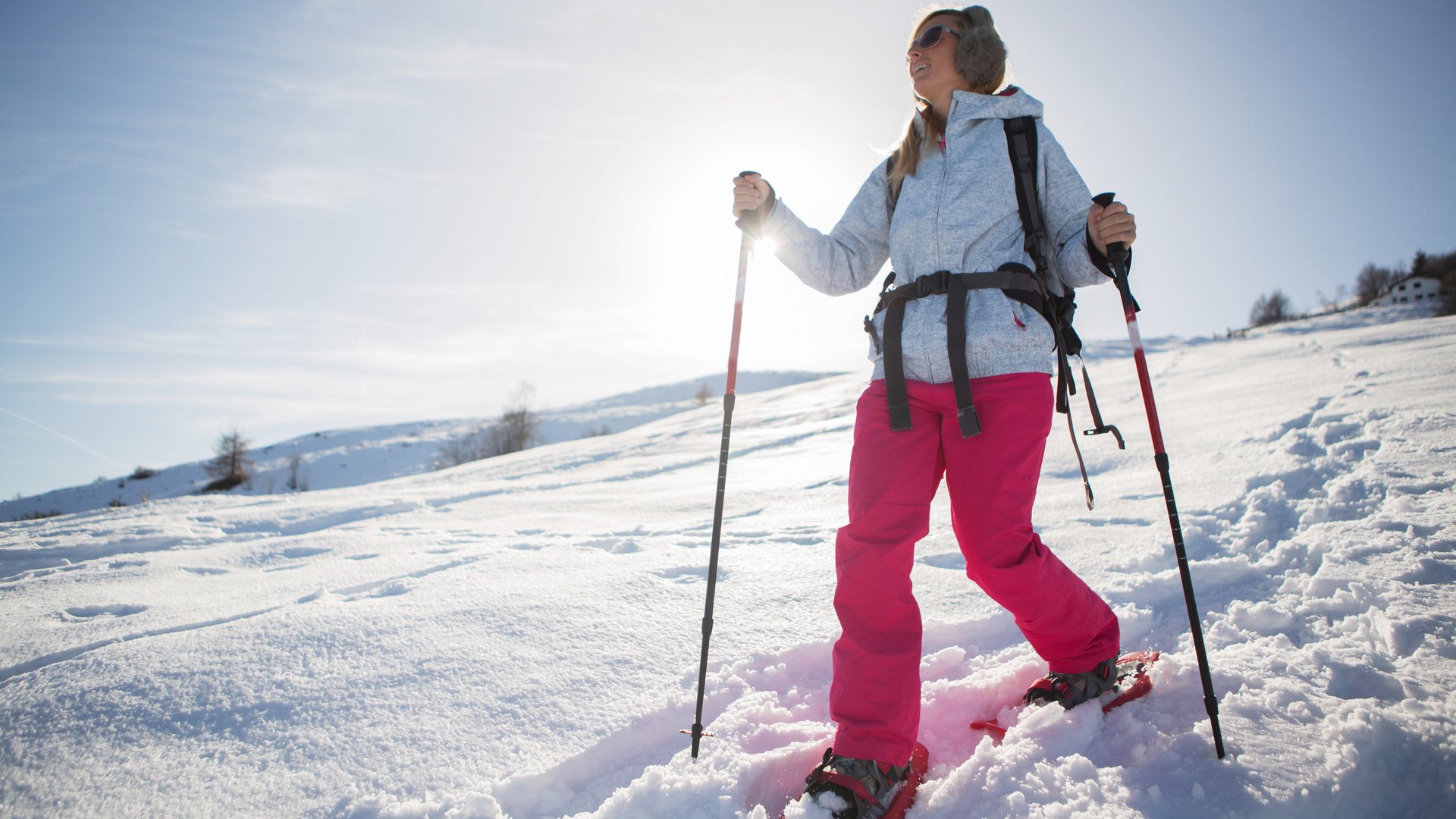 A woman snowshoeing in winter with all sport clothing equipment during a beautiful sunny day, going the way down,sun behind her.Winter in Switzerland.
