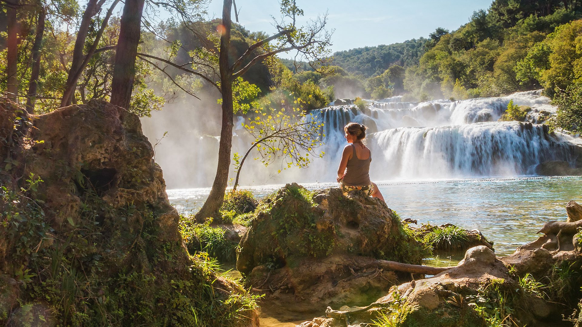 Beautiful woman sits at the waterfall in Krka national park, Croatia
