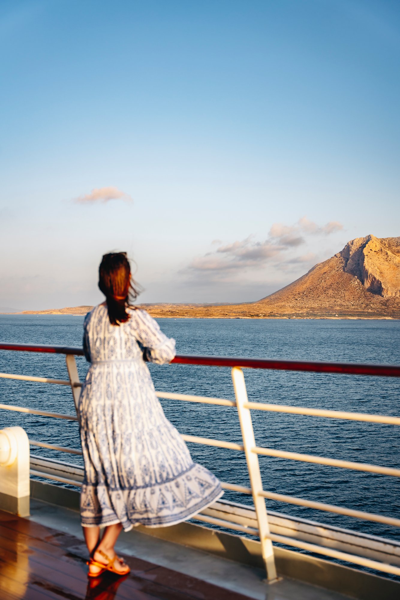 Frau steht an Reling und blickt aufs Meer