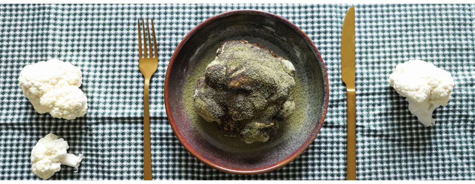 Al centro della tavola il cavolfiore e la salsa con alici sono ricoperti da una polvere di capperi