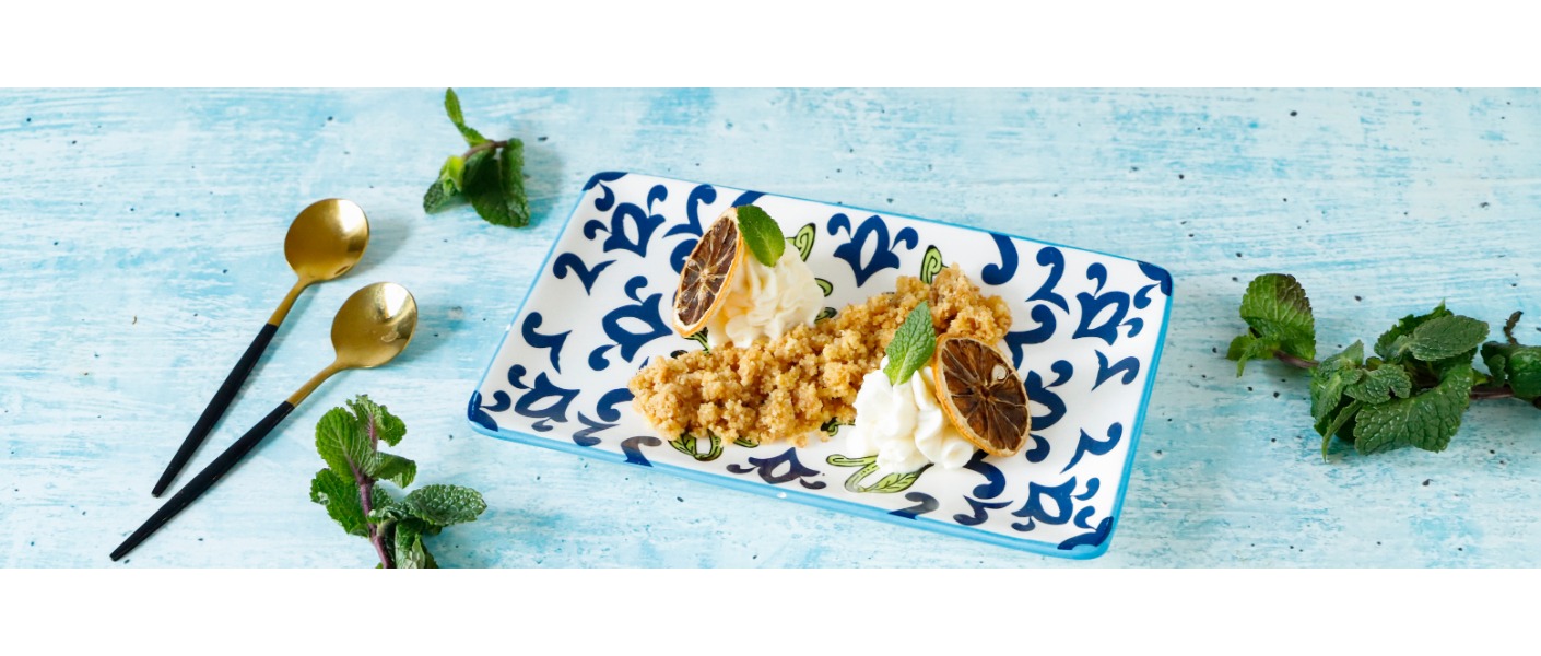 Cheesecake scomposta su un piatto rettangolare bianco e blu, decorata con fette di limone e foglie di menta