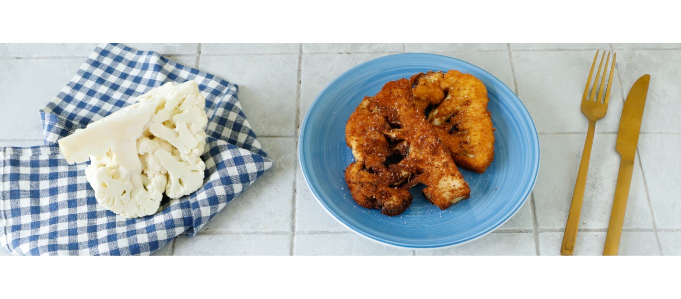 Una dorata fetta di cotoletta di cavolfiore su un piatto azzurro, cosparsa di sale fino