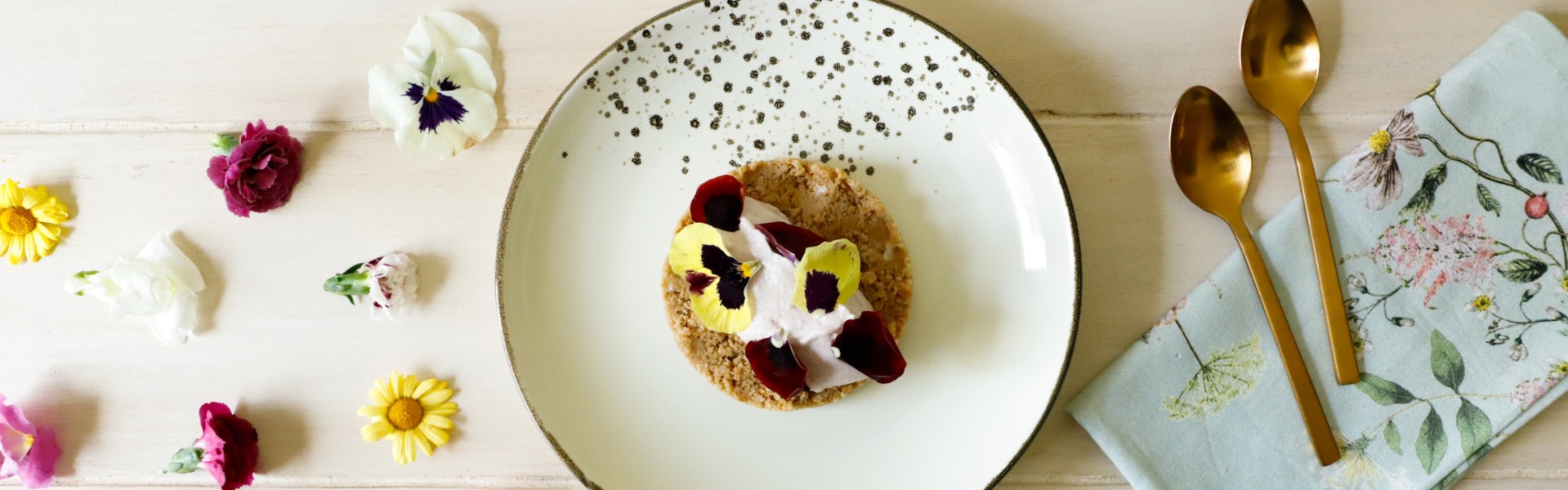 Dolce gourmet al piatto con base croccante di biscotti e burro e una quenelle di crema di ricotta e marmellata di ciliegie, decorato con fiori eduli